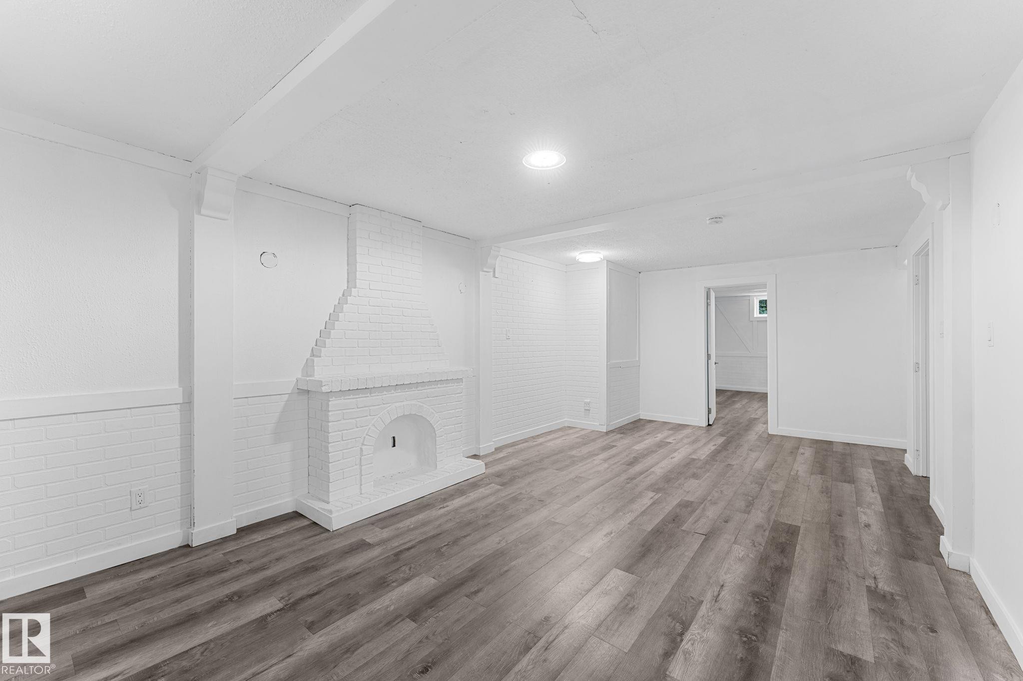 Spacious room featuring wood-finish flooring, a painted brick fireplace, recessed lighting, and white paneled walls - 7823 136 Avenue Nw, Edmonton, AB - Indoor Photo Showing Other Room