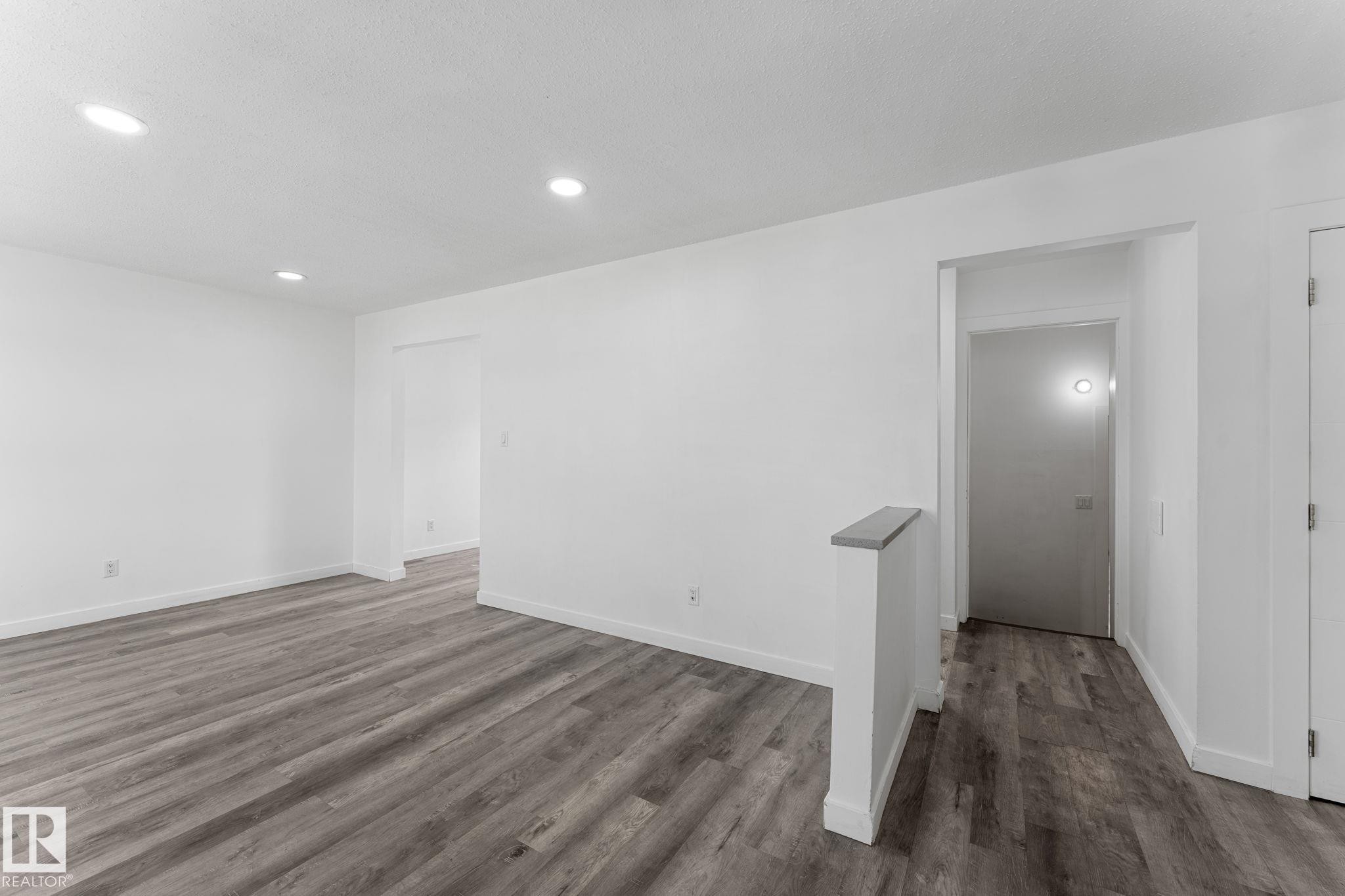 Recessed ceiling lighting, light gray wood-finish flooring, white painted walls, and a gray-capped half-wall - 7823 136 Avenue Nw, Edmonton, AB - Indoor Photo Showing Other Room
