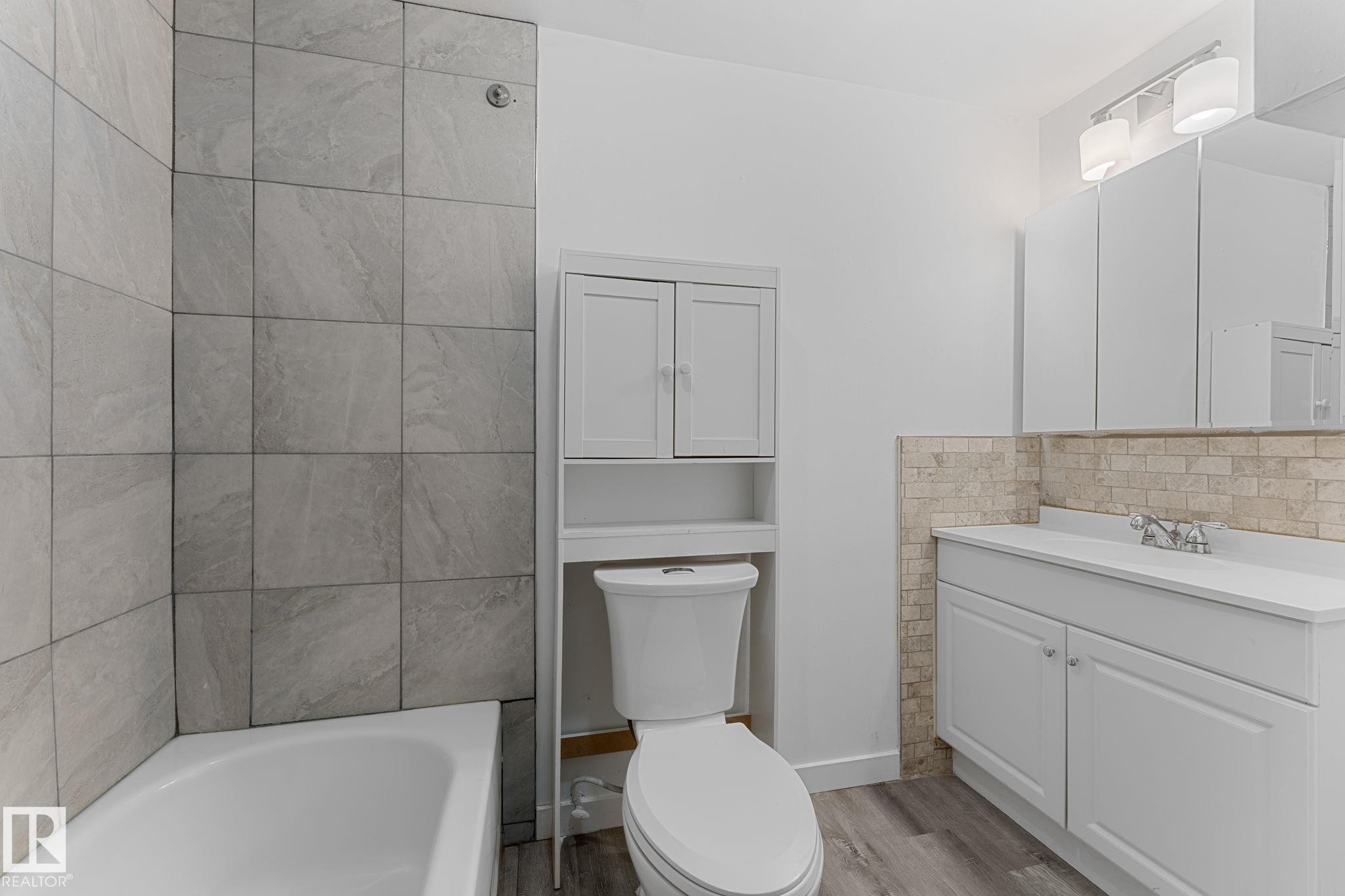 White vanity with an integrated sink, built-in storage cabinet, and stone tile backsplash - 7823 136 Avenue Nw, Edmonton, AB - Indoor Photo Showing Bathroom