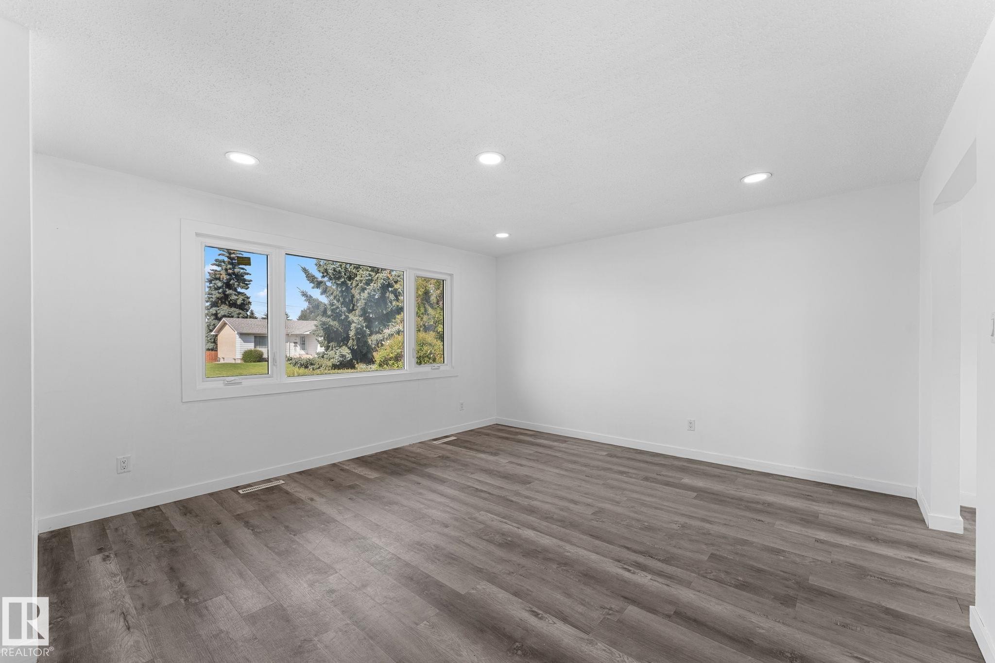 Spacious room featuring wood-finish flooring, recessed lighting, and a large multi-pane window - 7823 136 Avenue Nw, Edmonton, AB - Indoor Photo Showing Other Room