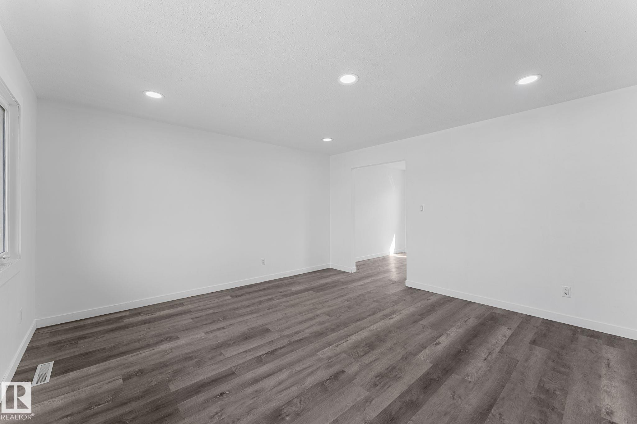 Recessed lighting illuminating the expansive room, featuring wood-finish flooring, white walls, and a window providing natural light - 7823 136 Avenue Nw, Edmonton, AB - Indoor Photo Showing Other Room