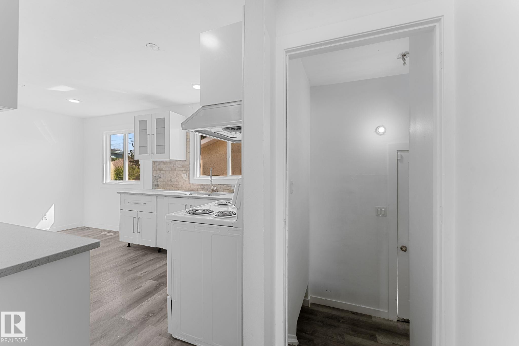 Kitchen featuring white cabinetry, light-toned countertops, a tile backsplash, and wood-finish flooring - 7823 136 Avenue Nw, Edmonton, AB - Indoor
