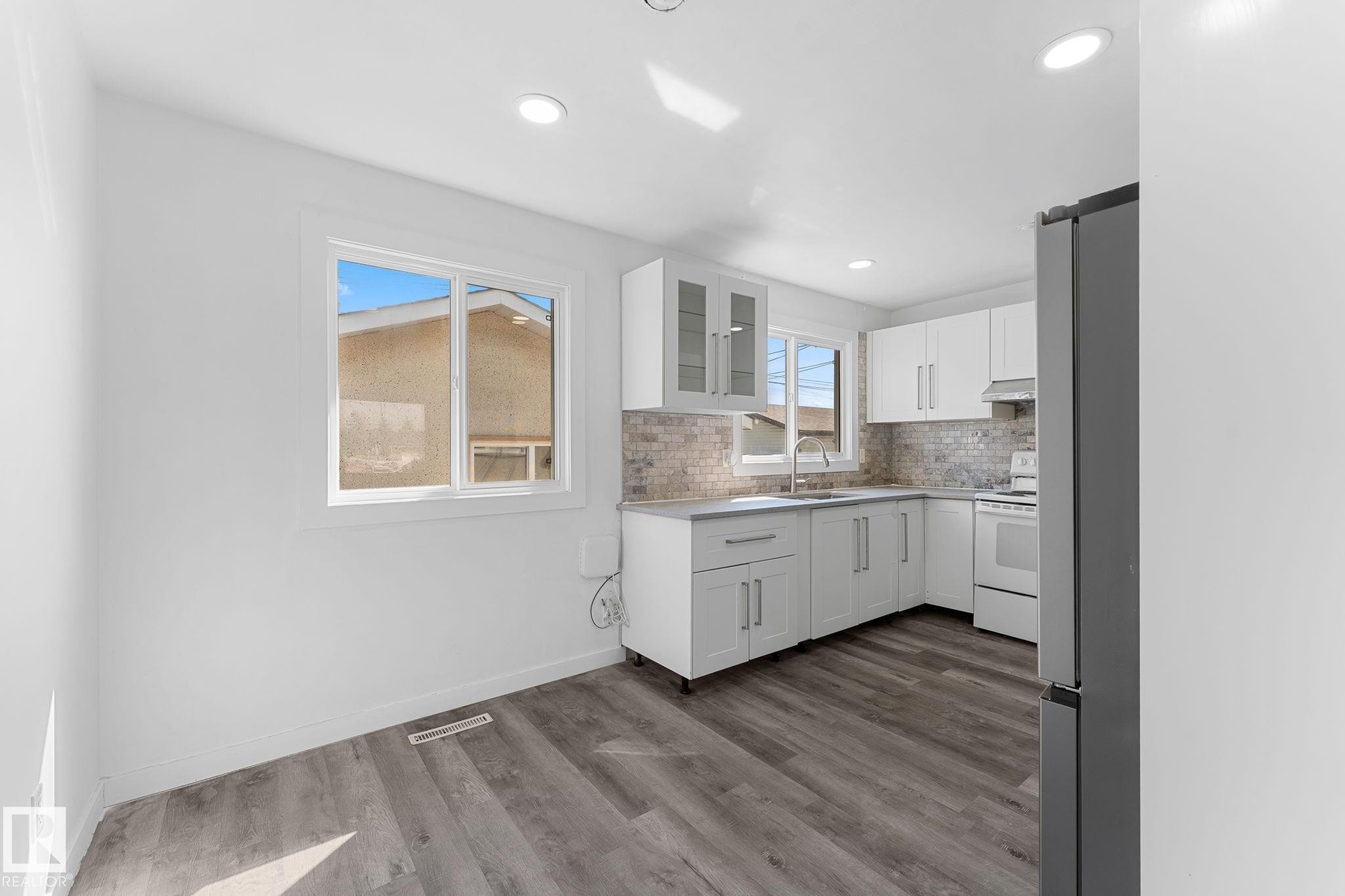 Kitchen featuring white shaker cabinetry, light-toned backsplash, gray wood-finish flooring, recessed lighting, and a stainless steel refrigerator - 7823 136 Avenue Nw, Edmonton, AB - Indoor Photo Showing Kitchen