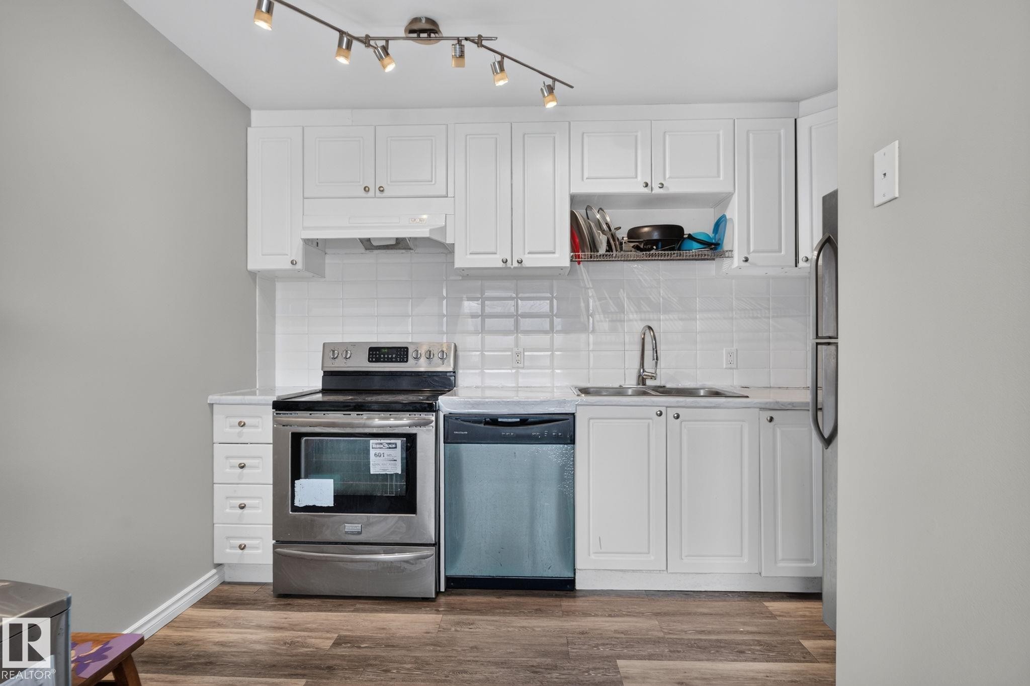 Bright kitchen featuring white cabinetry, subway tile backsplash, stainless steel appliances, and wood-finish flooring - 17775 95 Street Nw, Edmonton, AB - Indoor Photo Showing Kitchen With Double Sink