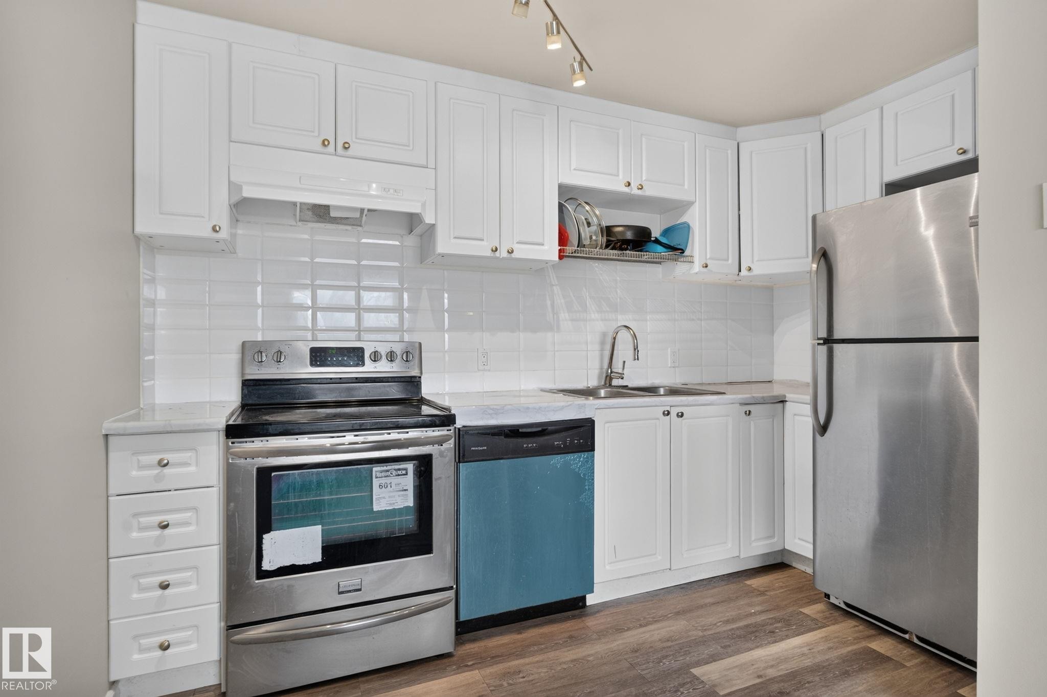 White shaker-style cabinetry, stainless steel appliances, wood-finish flooring, white subway tile backsplash, and track lighting - 17775 95 Street Nw, Edmonton, AB - Indoor Photo Showing Kitchen With Double Sink