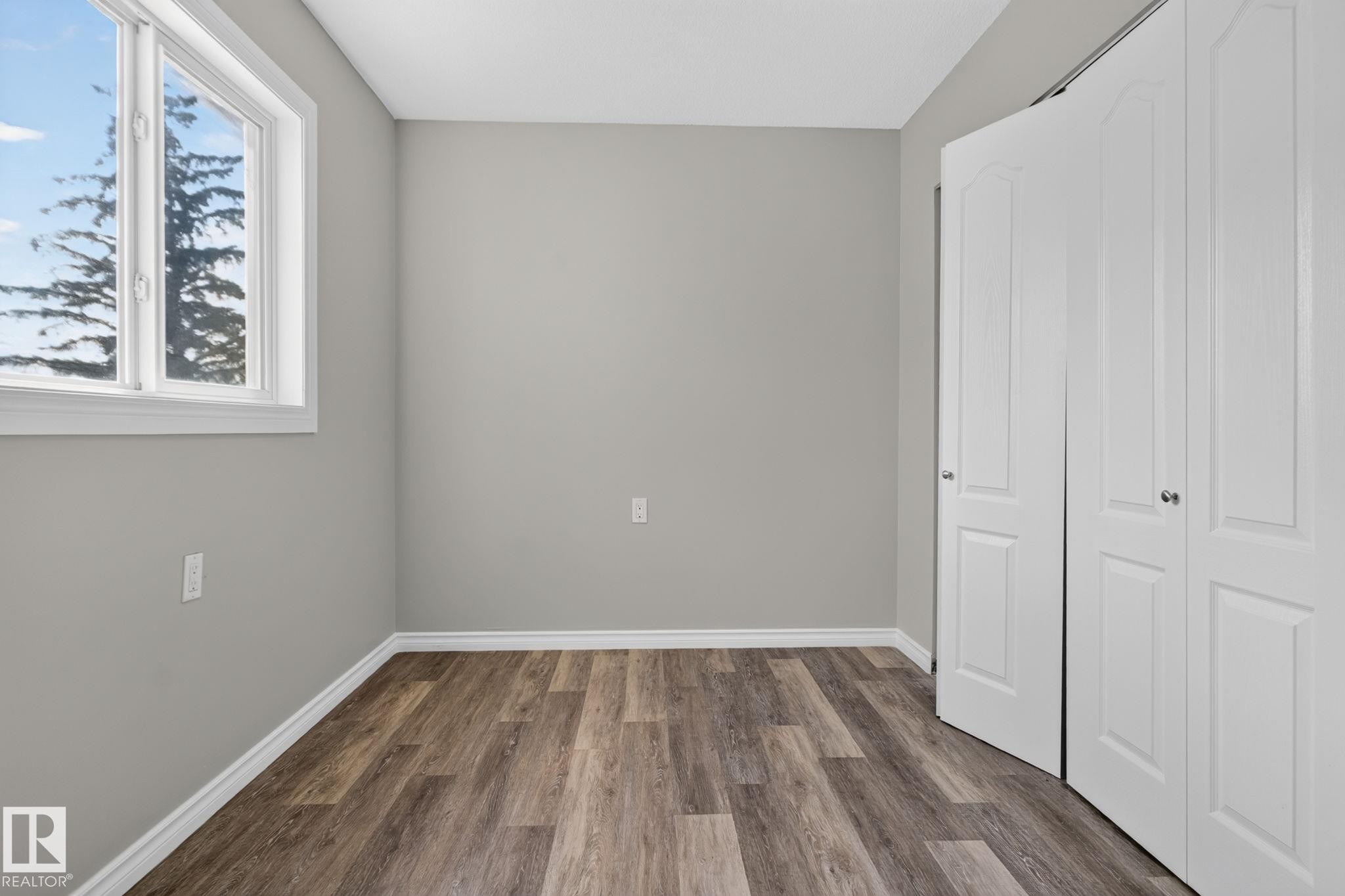 Light gray wall paint, wood-finish flooring, a white-framed window, and bi-fold closet doors - 17775 95 Street Nw, Edmonton, AB - Indoor Photo Showing Other Room