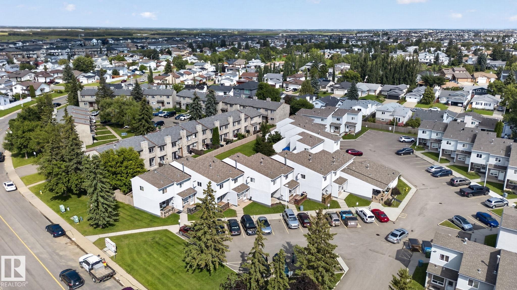 Aerial perspective showcasing a residential community with multiple townhome buildings, paved parking areas, and mature trees - 17775 95 Street Nw, Edmonton, AB - Outdoor With View