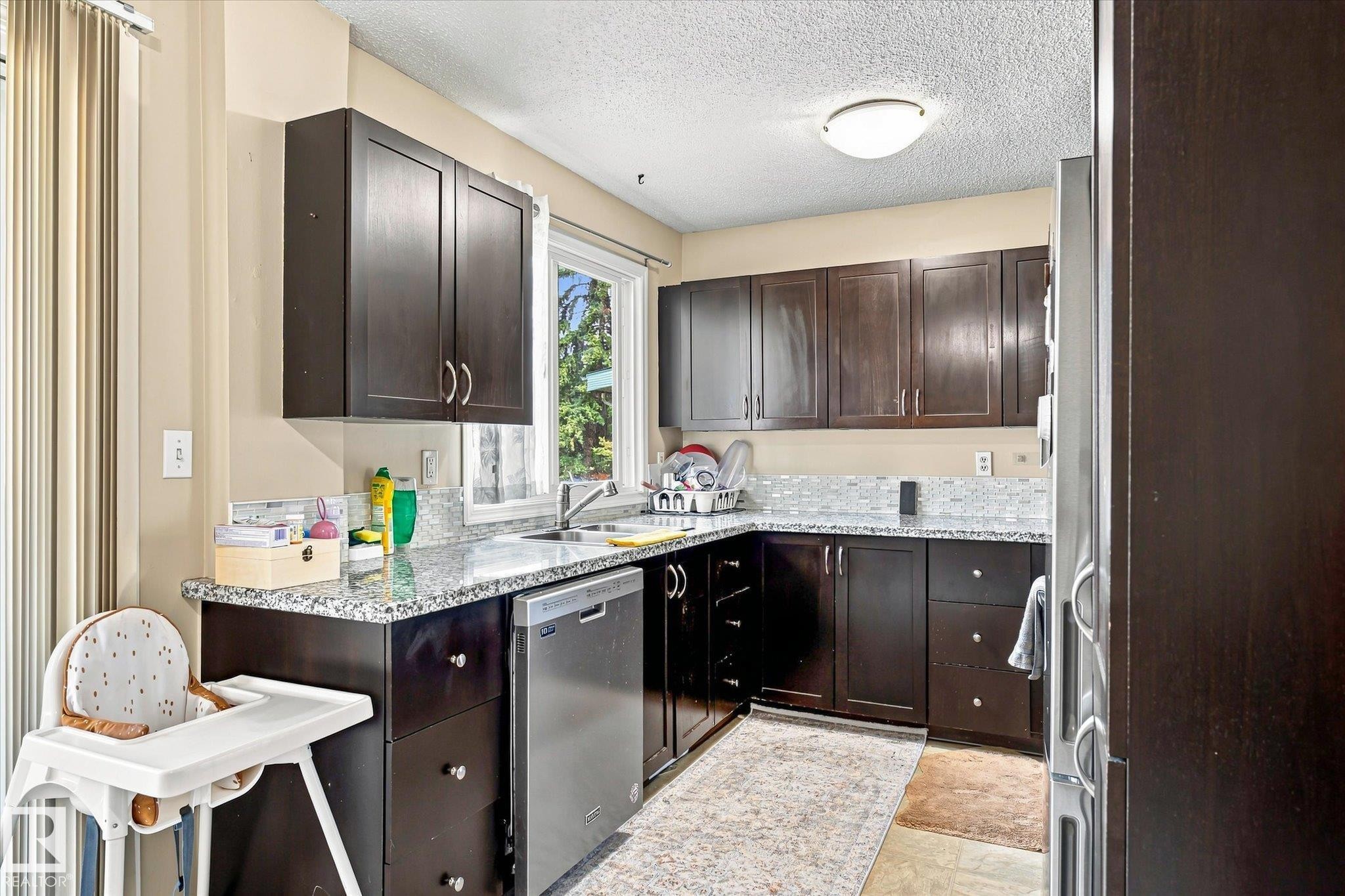 U-shaped kitchen with dark wood-finish cabinetry, light-colored granite countertops, and a mosaic tile backsplash - 6471 180 Street Nw, Edmonton, AB - Indoor Photo Showing Kitchen