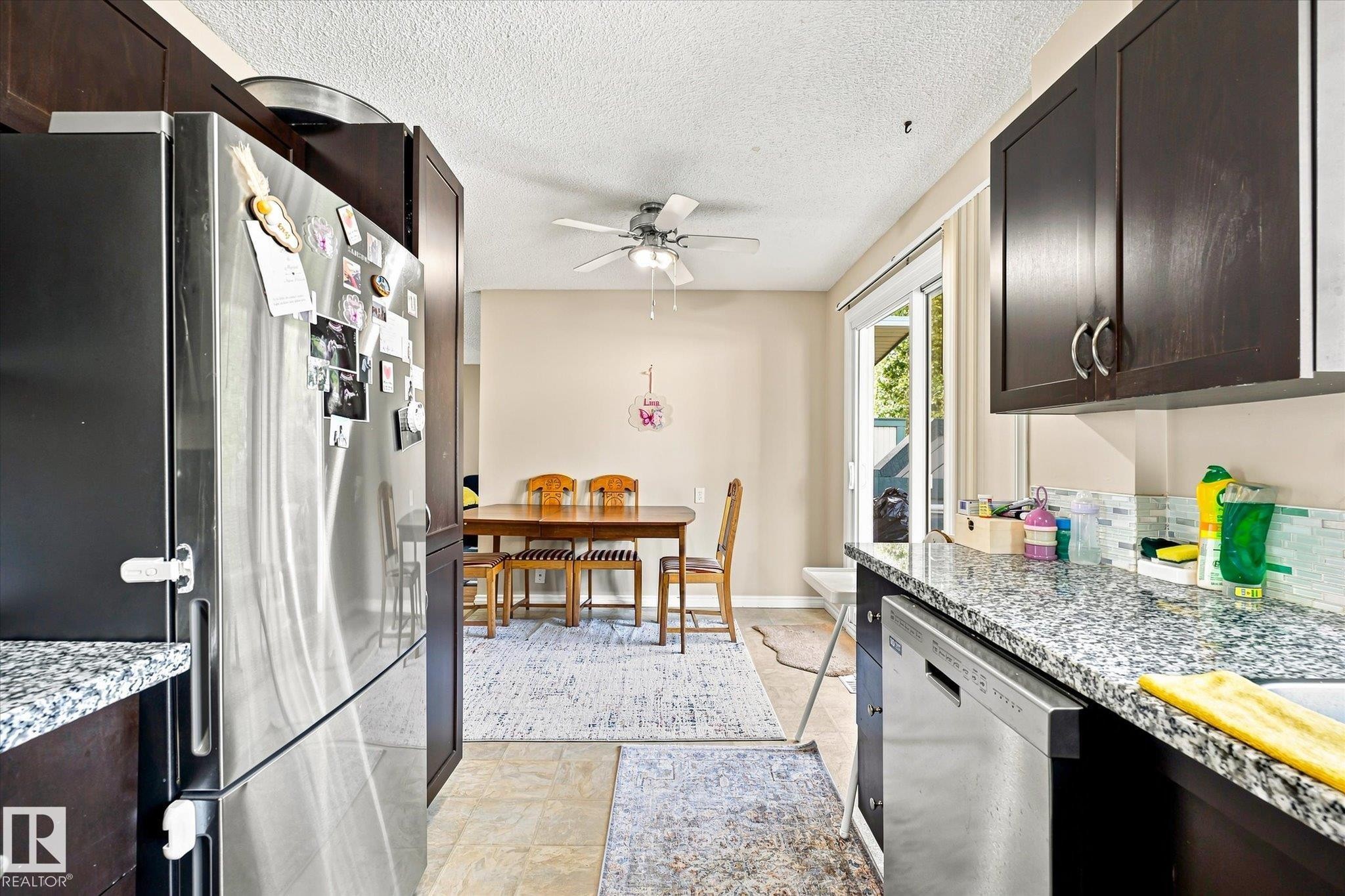 Kitchen featuring dark wood-finish cabinetry, light speckled countertops, a tile backsplash, and stainless steel appliances - 6471 180 Street Nw, Edmonton, AB - Indoor Photo Showing Kitchen