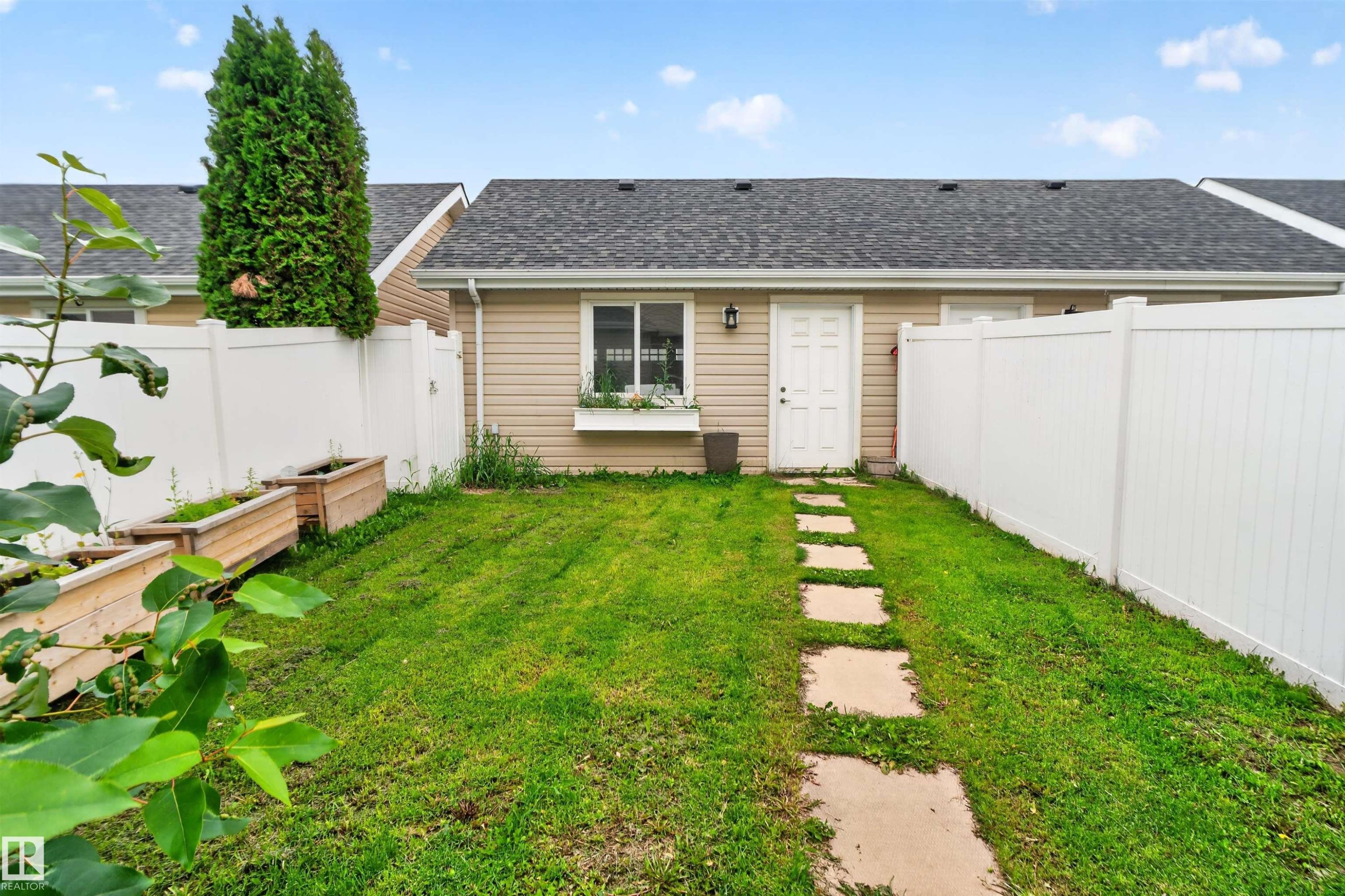 Backyard featuring a privacy fence, manicured lawn, stone pathway, and raised garden beds - 4471 Mccrae Avenue Nw, Edmonton, AB