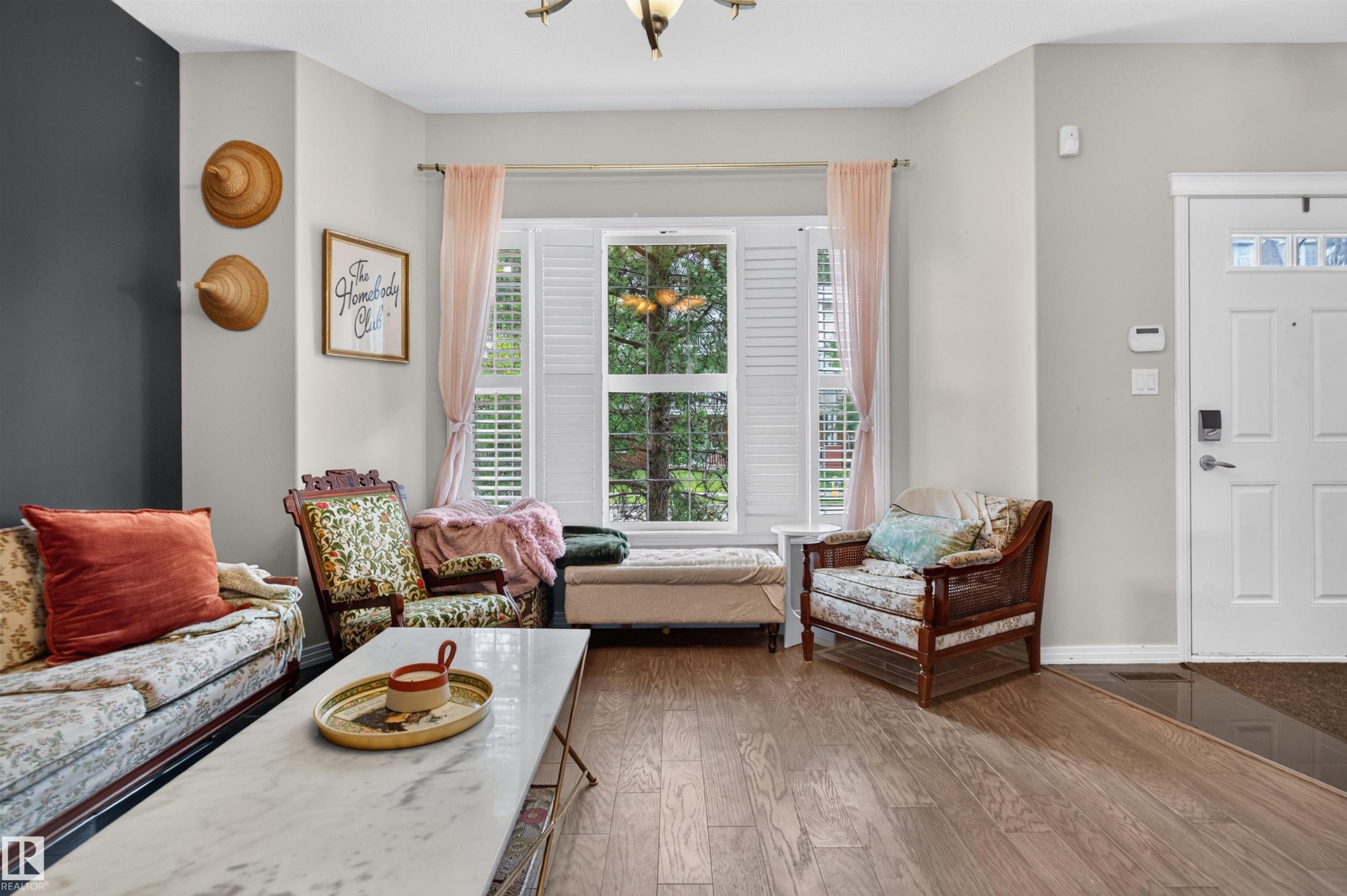 Wood-finish flooring, bay window with plantation shutters, white paneled entry door with decorative glass inserts, and a decorative light fixture - 4471 Mccrae Avenue Nw, Edmonton, AB