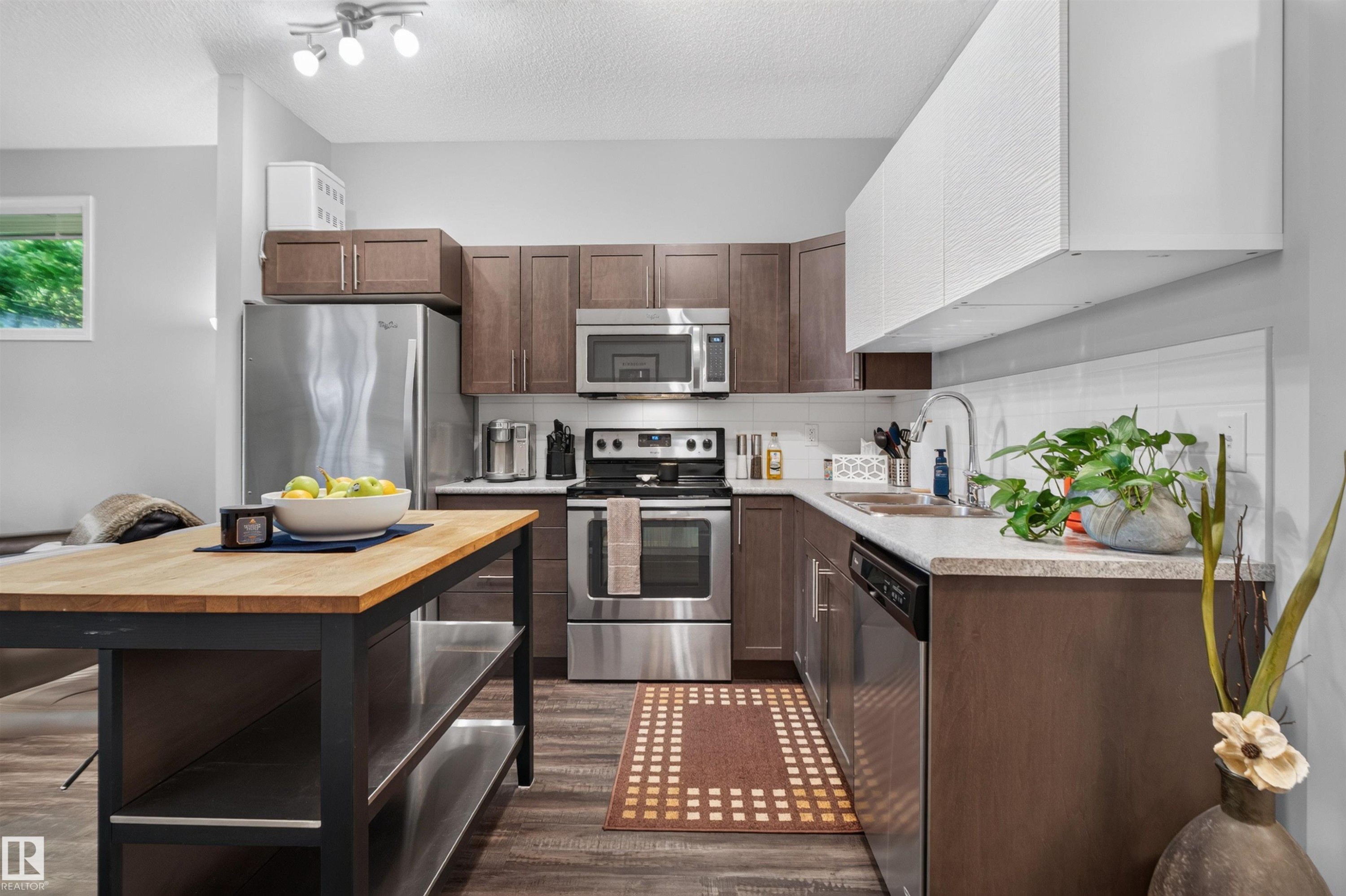 Contemporary kitchen featuring stainless steel appliances, wood-finish cabinetry, light-toned countertops, and a white subway tile backsplash - #34 6520 2 Av Sw, Edmonton, AB - Indoor Photo Showing Kitchen With Stainless Steel Kitchen With Upgraded Kitchen