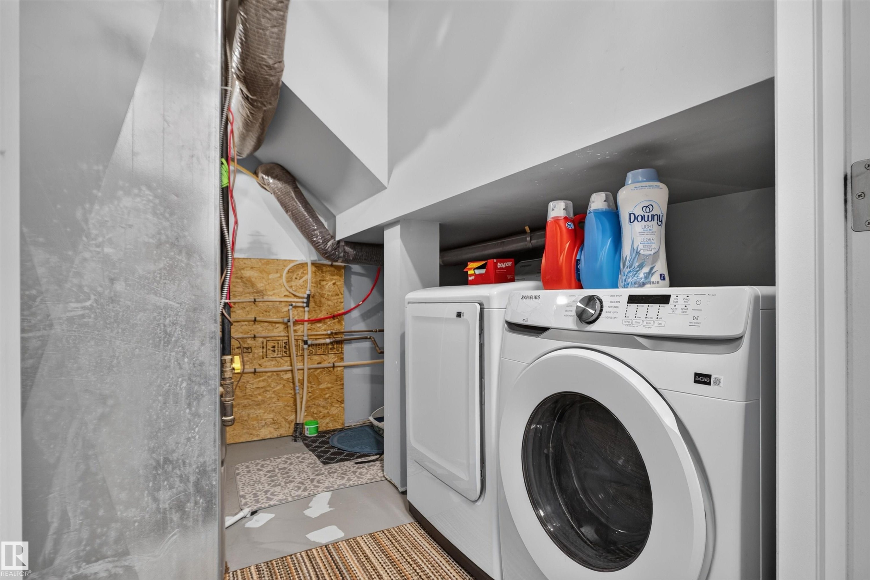 Laundry area featuring a stackable washer and dryer, adjacent utility access, and overhead shelving - #34 6520 2 Av Sw, Edmonton, AB - Indoor Photo Showing Laundry Room