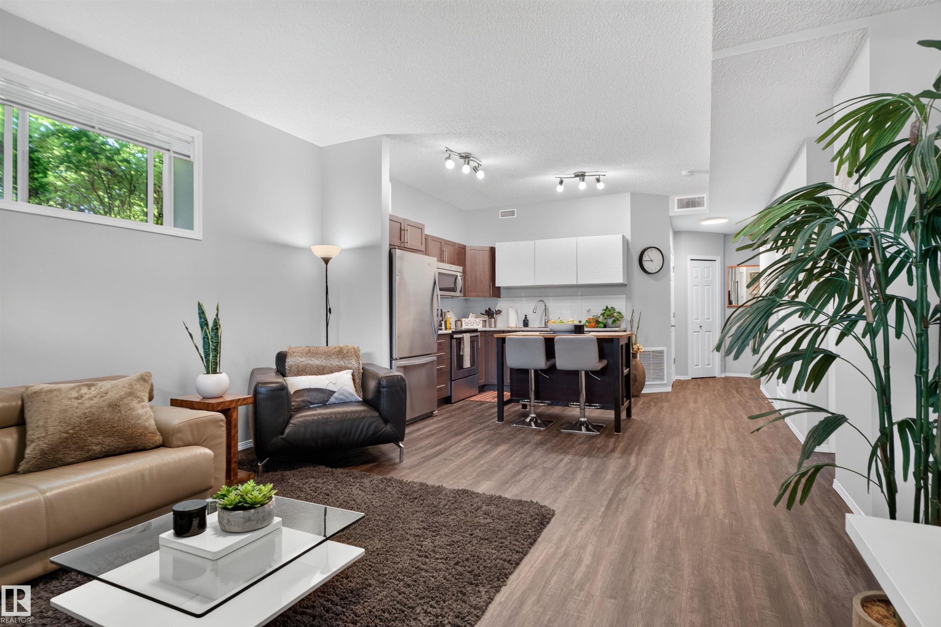 Open-concept living area featuring wood-finish flooring, recessed lighting, and a kitchen with stainless steel appliances - #34 6520 2 Av Sw, Edmonton, AB - Indoor Photo Showing Living Room
