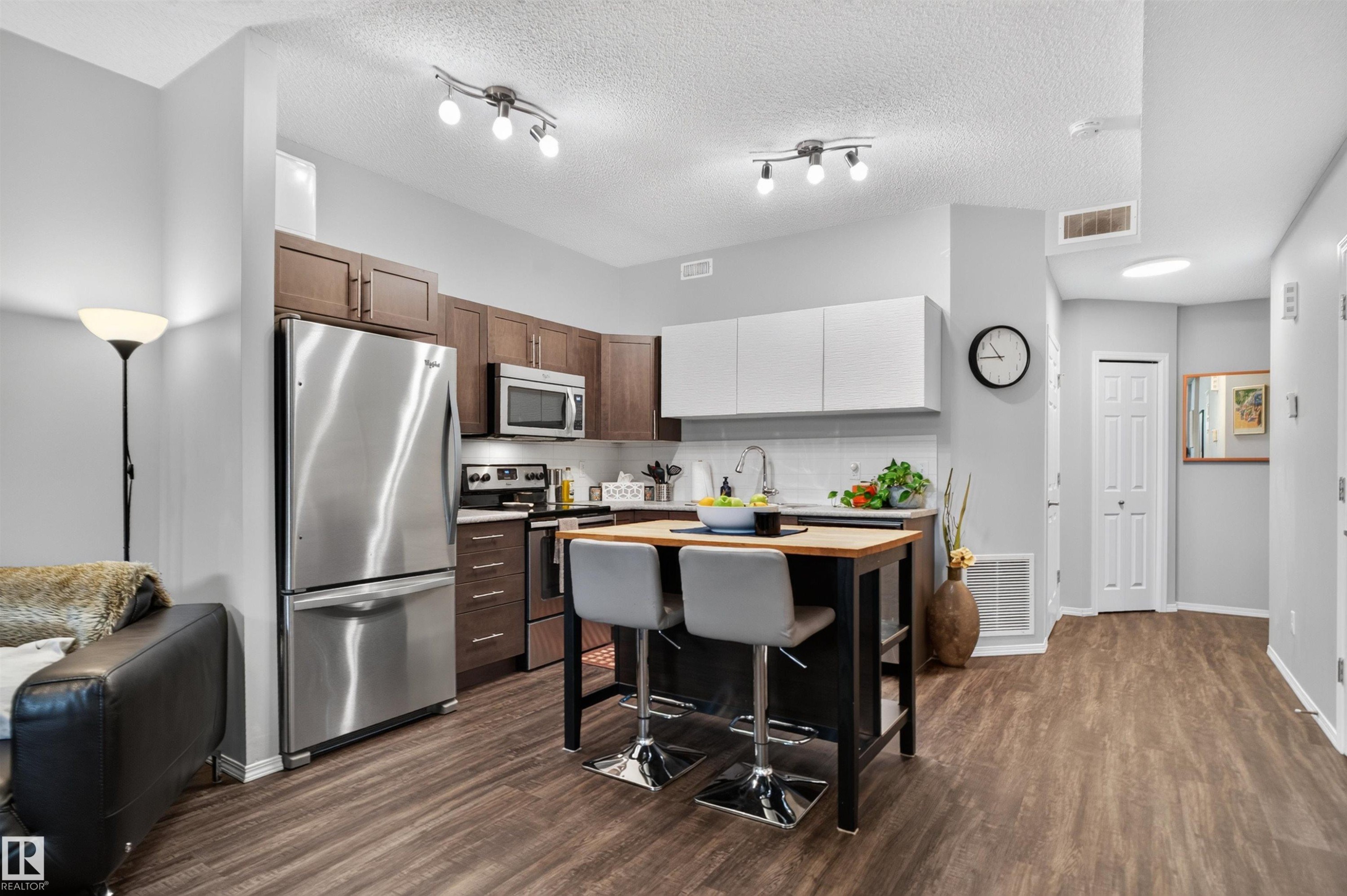 Modern kitchen featuring stainless steel appliances, two-tone cabinetry, a central island with seating, and wood-finish flooring - #34 6520 2 Av Sw, Edmonton, AB - Indoor Photo Showing Kitchen With Stainless Steel Kitchen