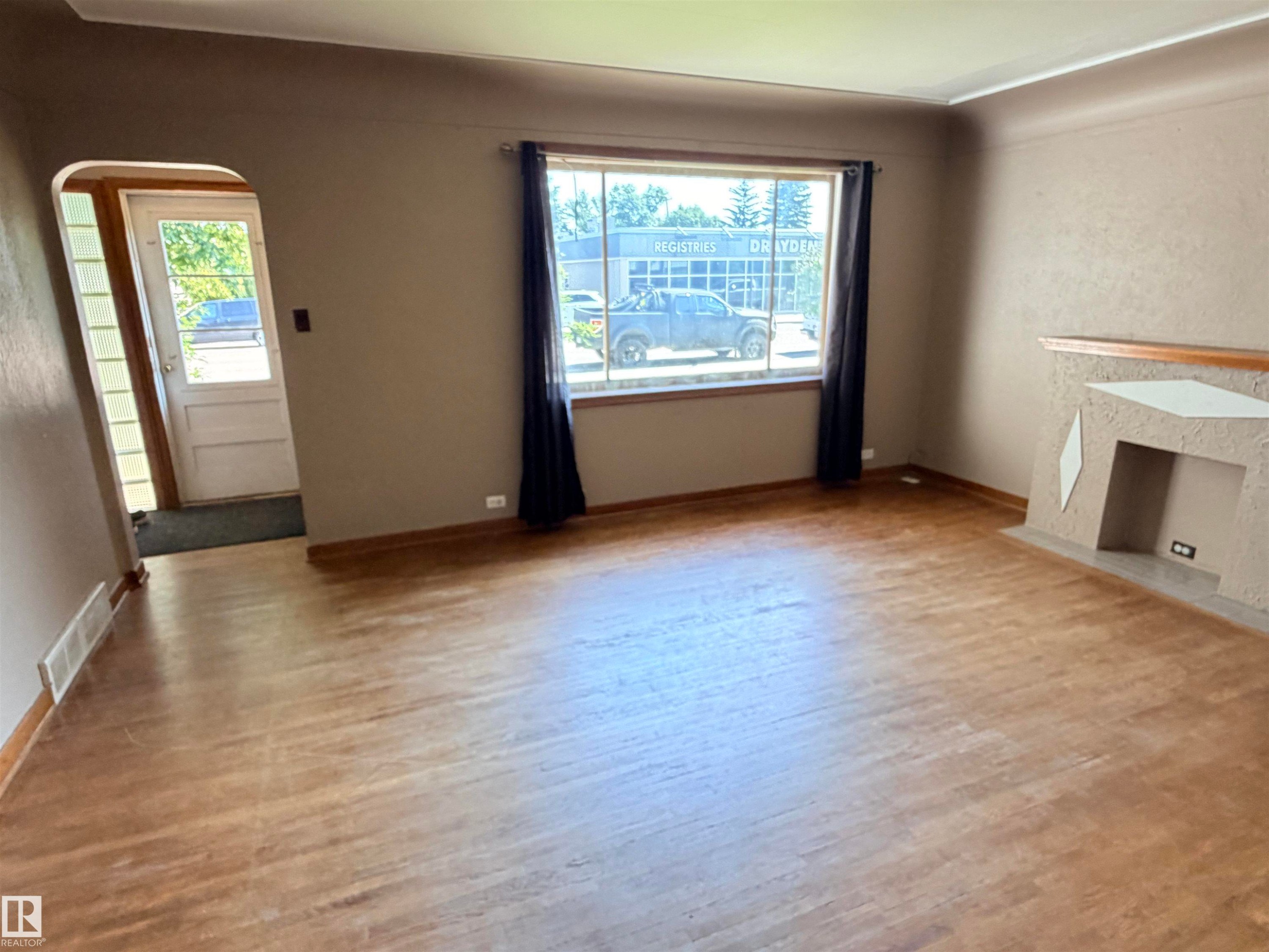 Wood-finish flooring throughout, a large window, and an integrated fireplace structure - 10416 100 Avenue, Westlock, AB - Indoor Photo Showing Other Room