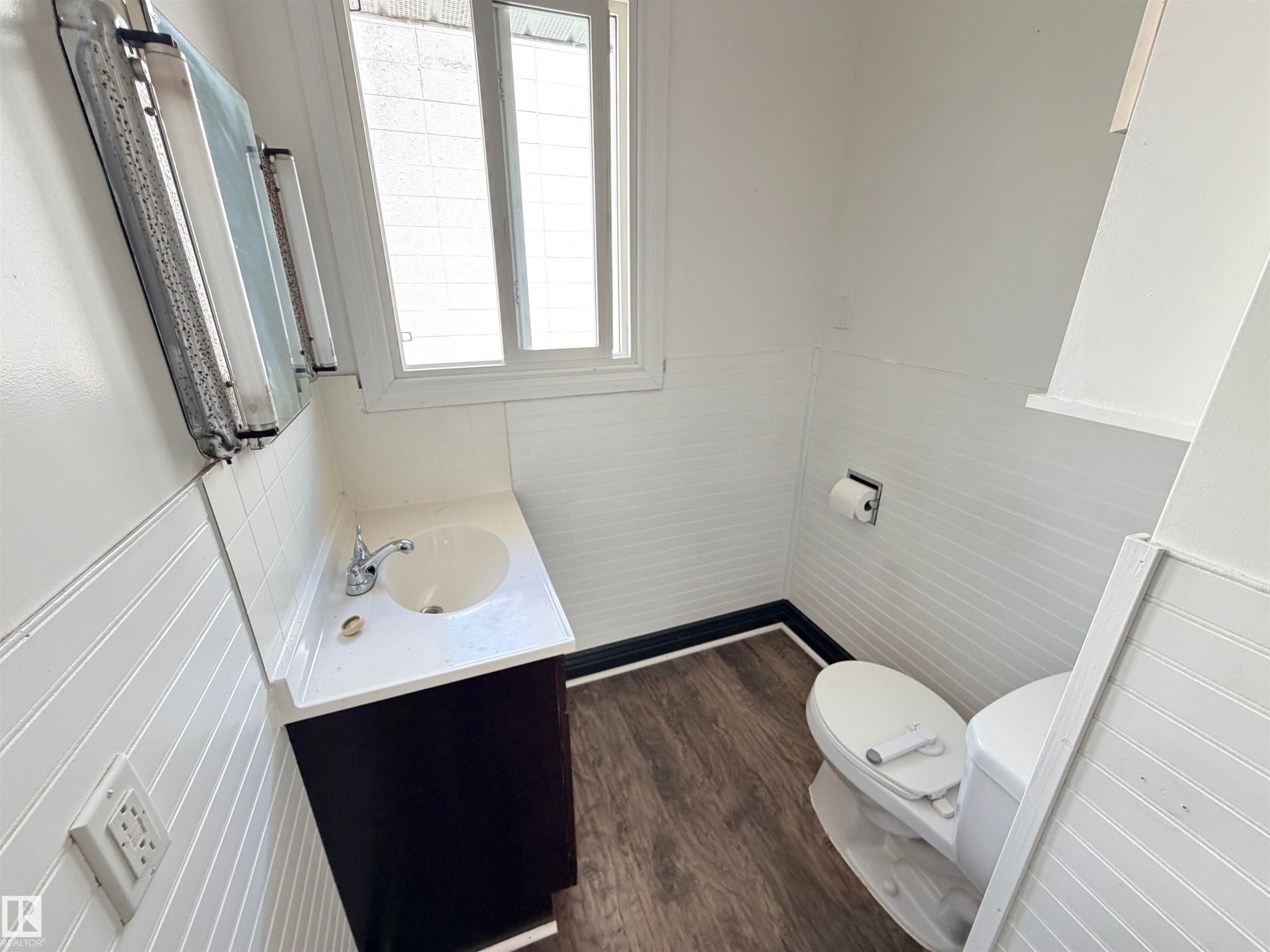 White tile wainscoting and beadboard paneling, wood-finish flooring, white vanity with integrated sink, and dual-pane window - 10416 100 Avenue, Westlock, AB - Indoor Photo Showing Bathroom