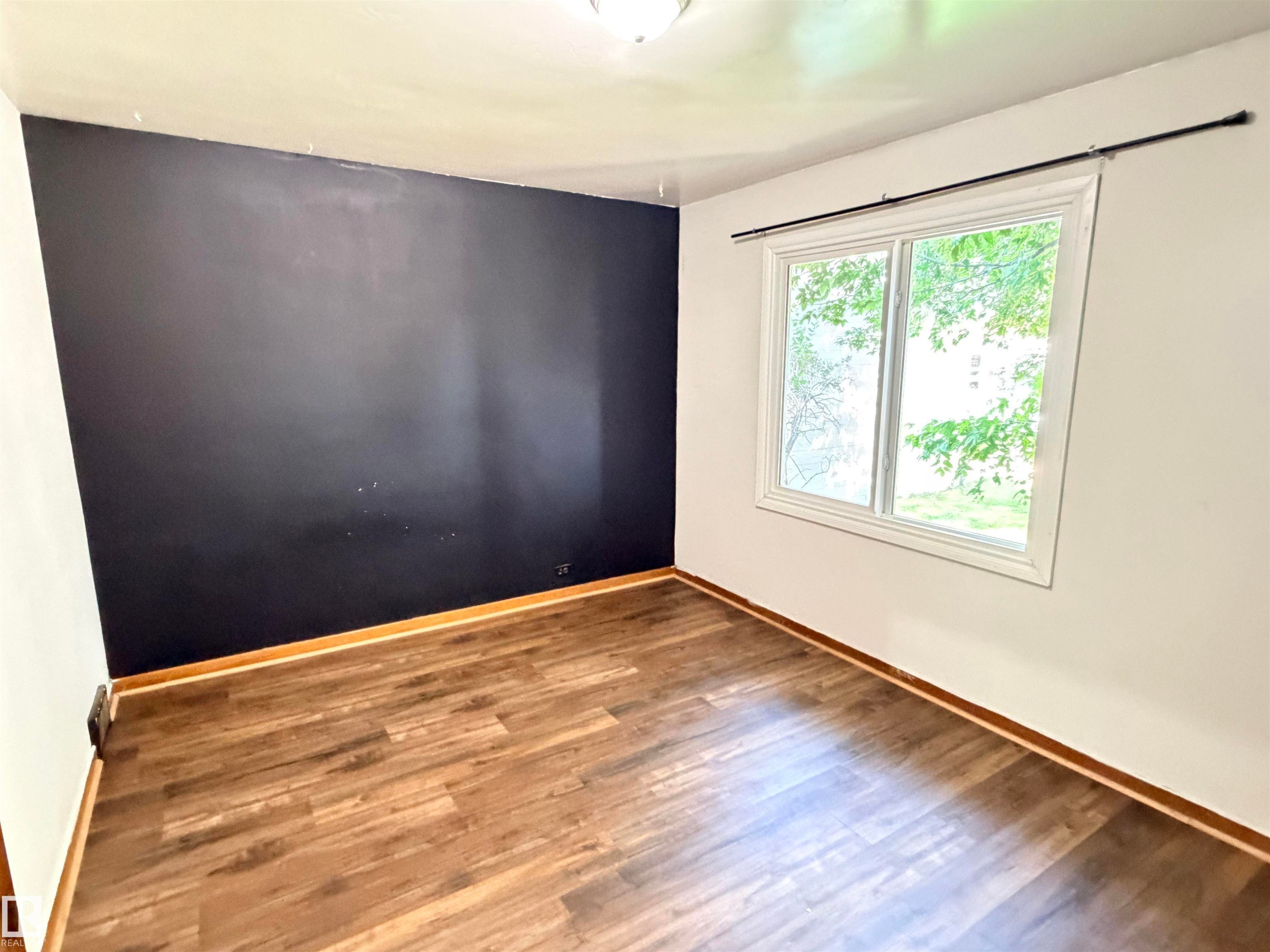 Wood-finish flooring with a contrasting dark accent wall and white painted walls - 10416 100 Avenue, Westlock, AB - Indoor Photo Showing Other Room