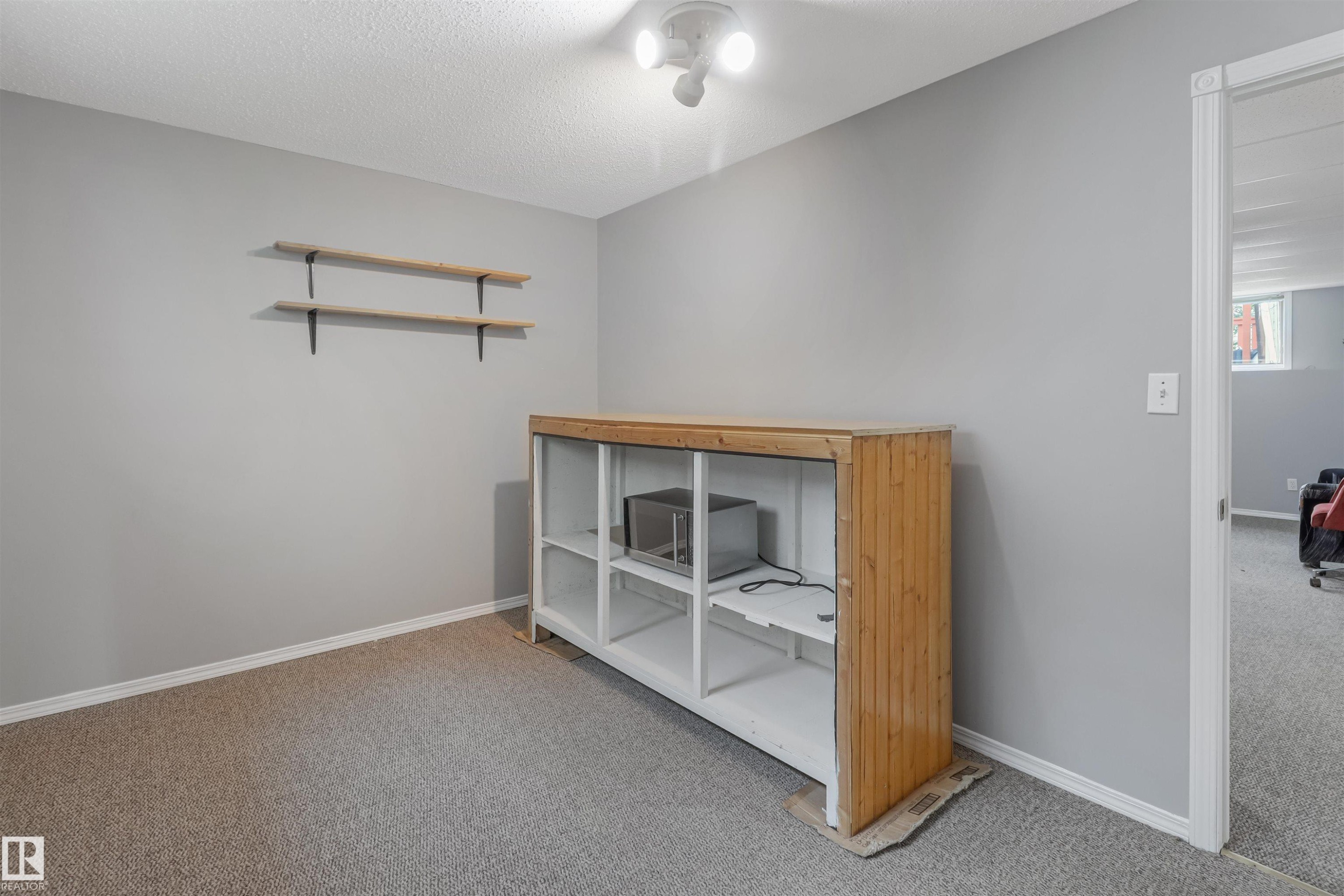 Light gray walls, carpet flooring, wooden built-in shelving, two wall-mounted wooden shelves, and an overhead track light fixture - 1055 Jones Crescent Nw, Edmonton, AB - Indoor Photo Showing Other Room