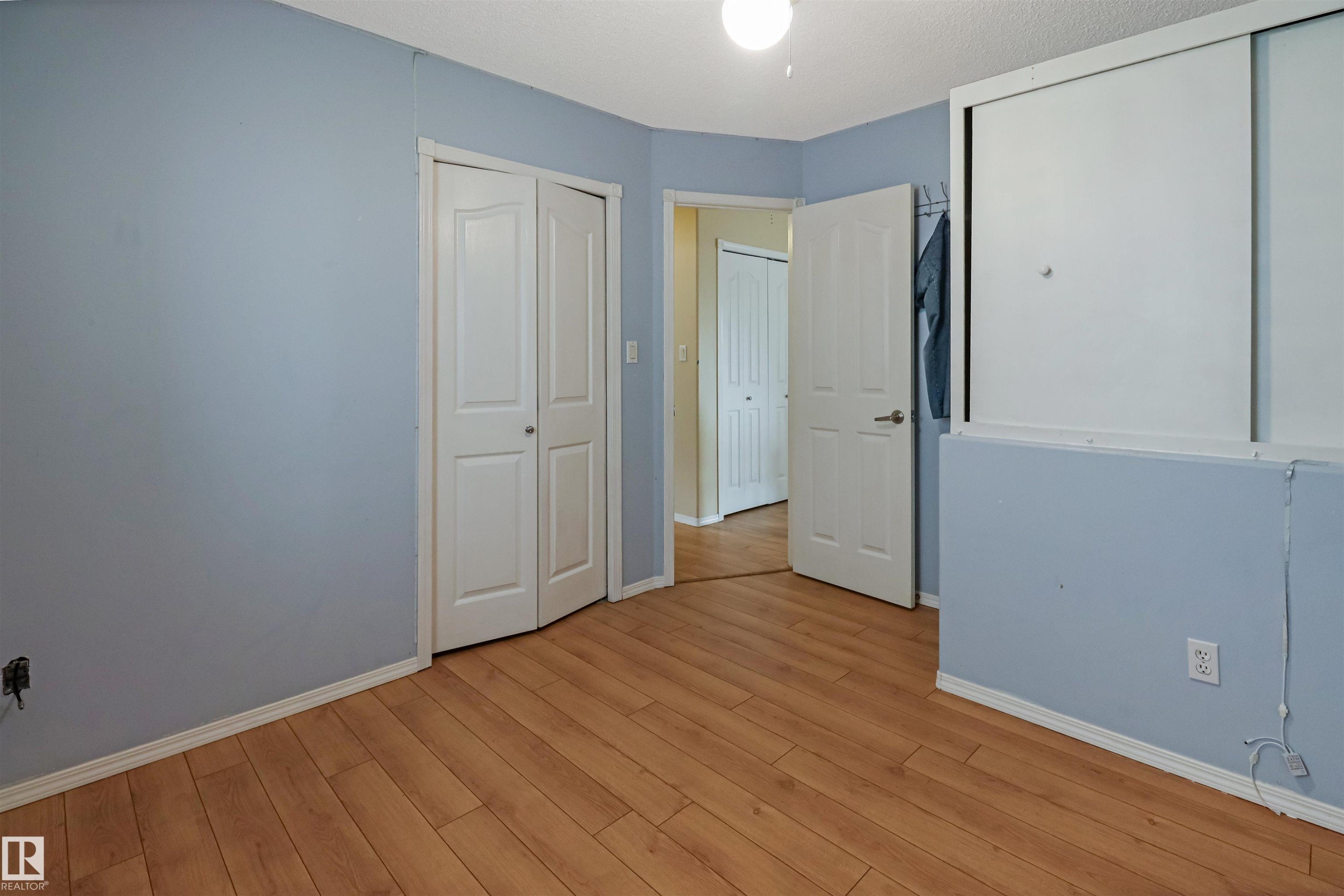 Spacious bedroom with soft blue walls, warm wood-finish flooring, and multiple closet options including mirrored sliding door storage - 1055 Jones Crescent Nw, Edmonton, AB - Indoor Photo Showing Other Room