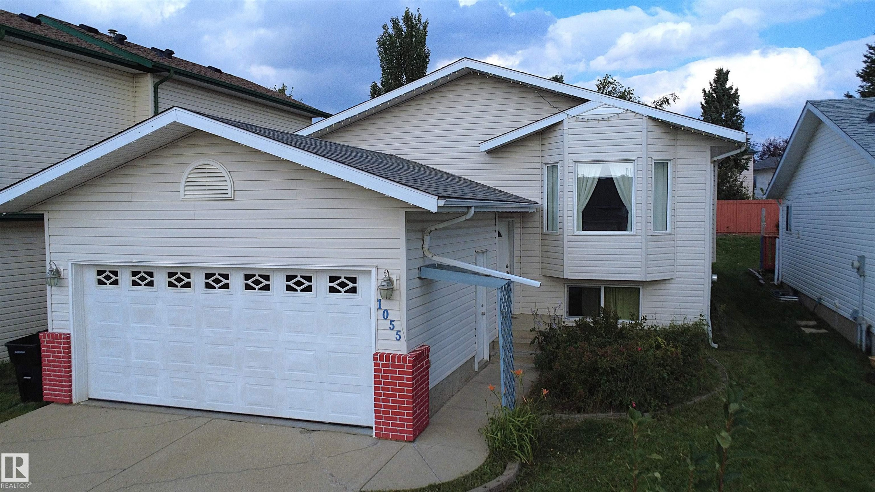 Front exterior featuring light-colored horizontal siding, a white panel garage door with decorative inserts, a bay window, and a concrete driveway - 1055 Jones Crescent Nw, Edmonton, AB - Outdoor With Exterior