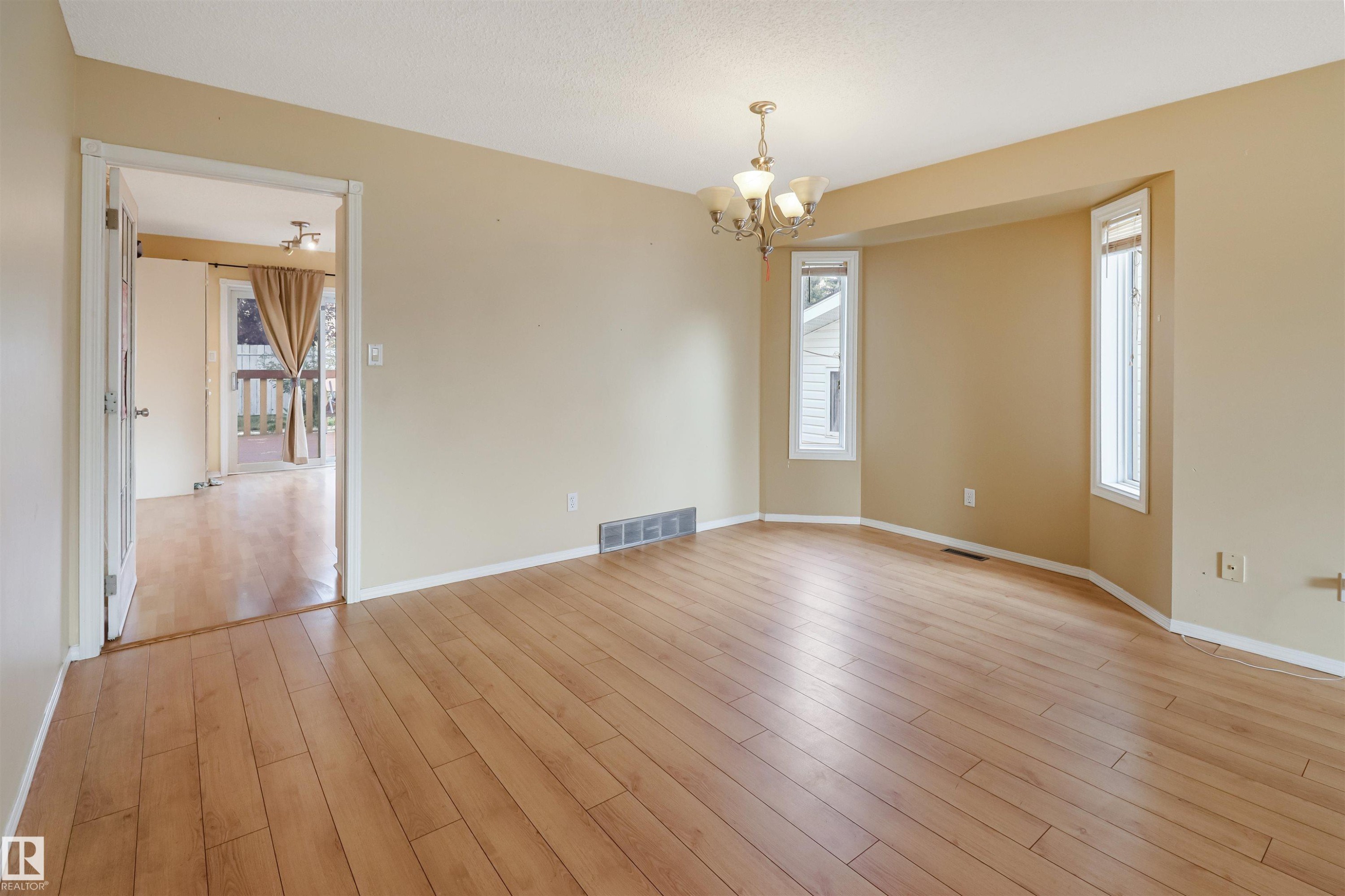 Spacious living room showcasing gleaming wood-finish flooring, warm neutral walls, and abundant natural light from multiple windows - 1055 Jones Crescent Nw, Edmonton, AB - Indoor Photo Showing Other Room