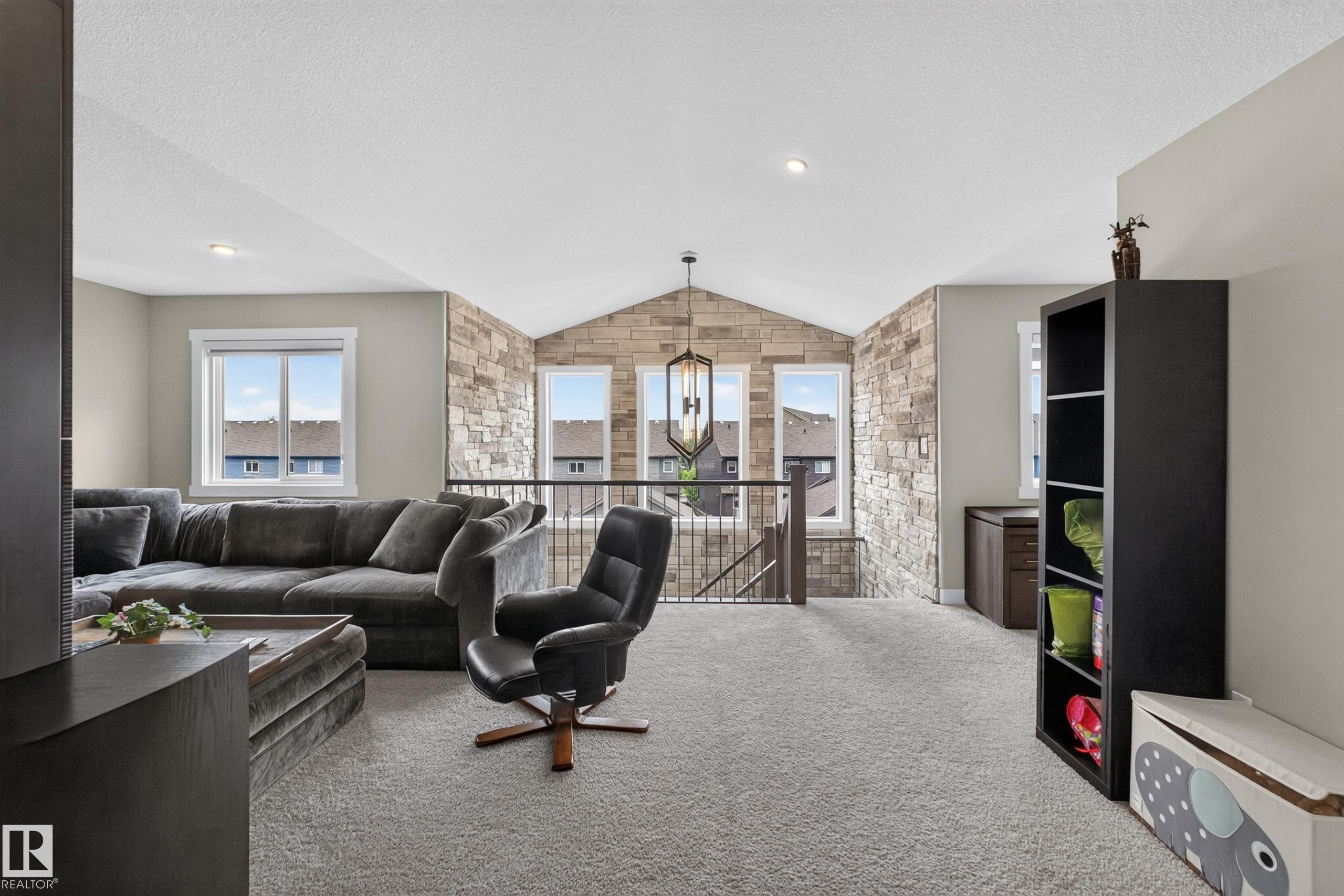 Carpeted loft space featuring an exposed stone accent wall, vaulted ceiling, and built-in shelving - 1399 Graydon Hill Way Sw, Edmonton, AB