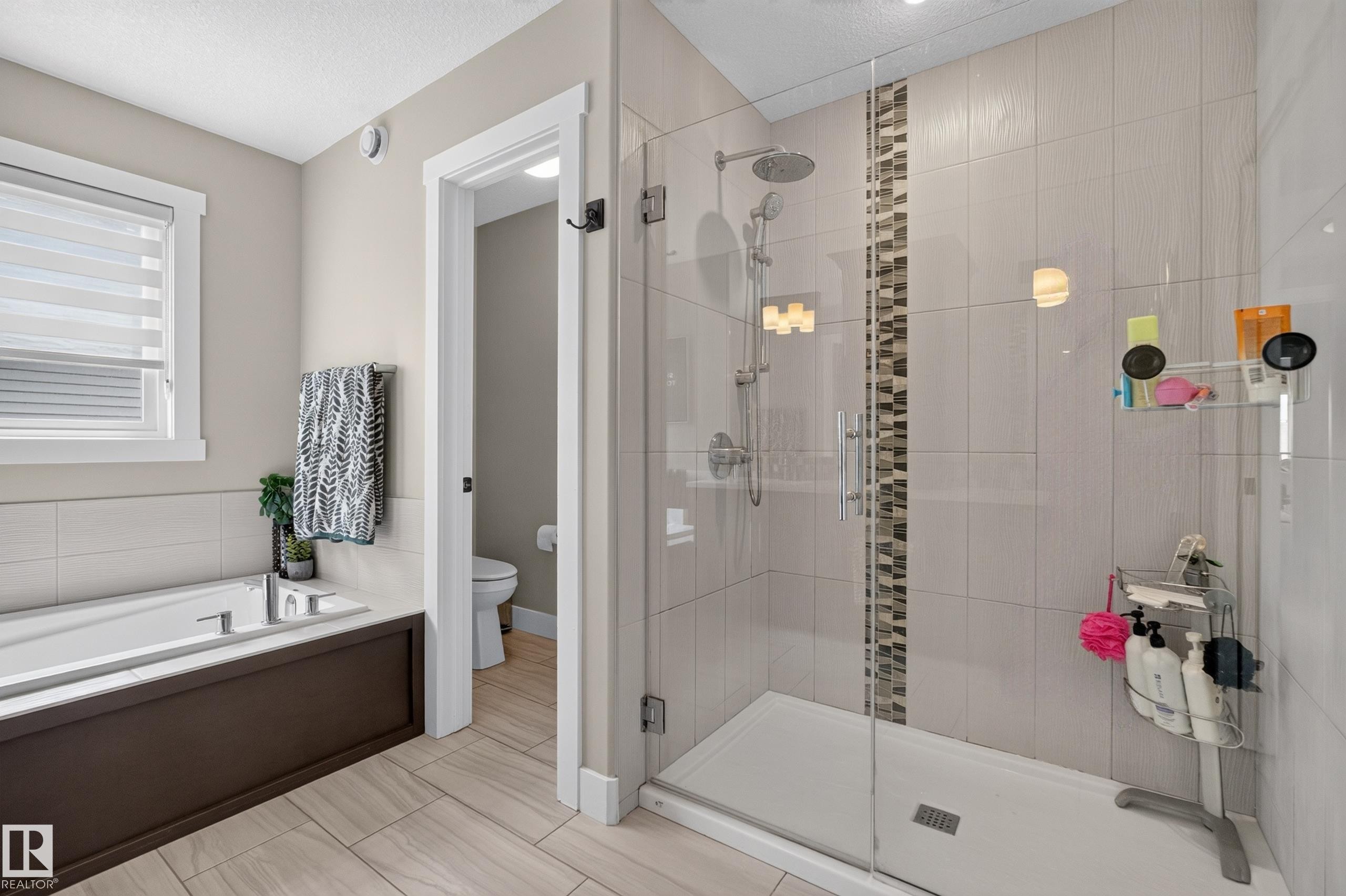 Fully tiled shower with a glass enclosure, rain showerhead, and a decorative tile accent strip - 1399 Graydon Hill Way Sw, Edmonton, AB