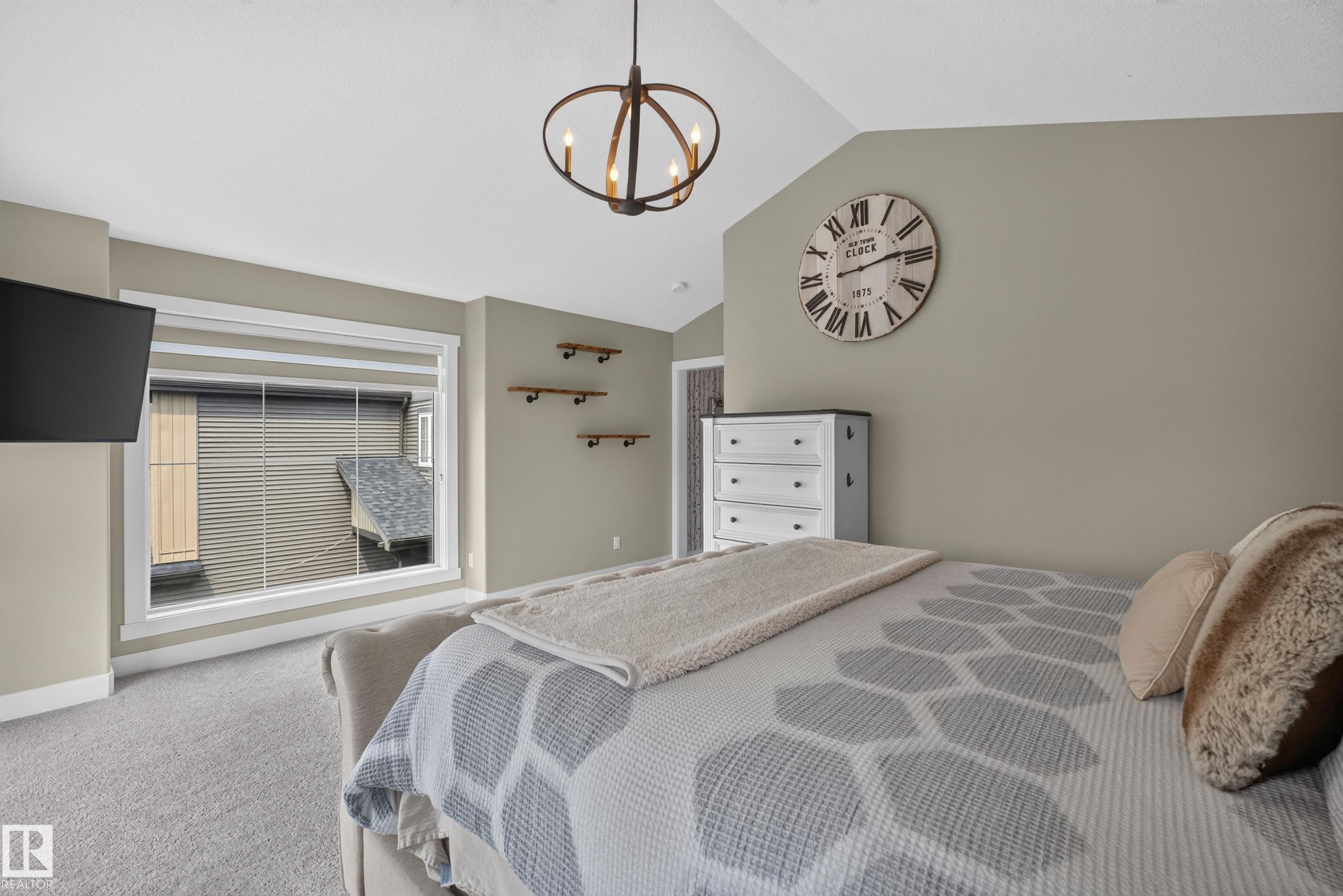 Vaulted ceiling with an industrial-style chandelier, large window with white trim, wall-mounted shelving, and carpet flooring - 1399 Graydon Hill Way Sw, Edmonton, AB