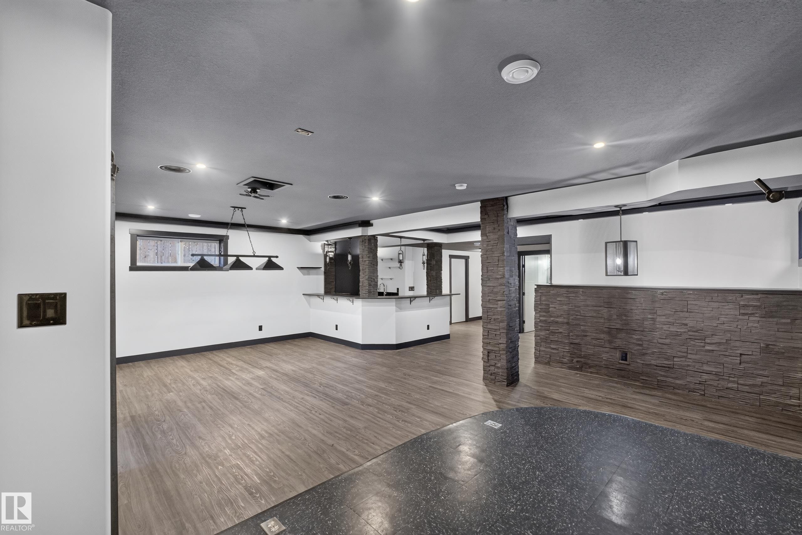 Expansive entertainment area featuring wood-finish flooring, recessed lighting, and a stone accent wall - 1399 Graydon Hill Way Sw, Edmonton, AB