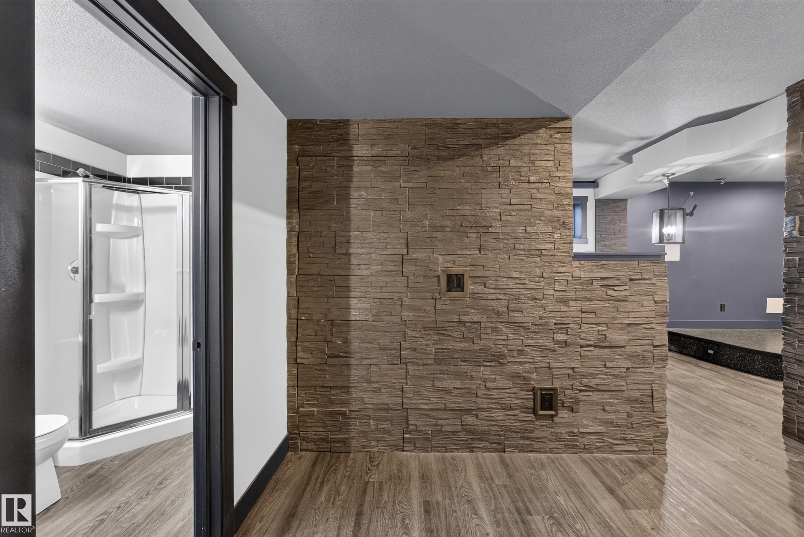 Stone accent wall, wood-finish flooring, full bathroom with shower, and contemporary pendant lighting - 1399 Graydon Hill Way Sw, Edmonton, AB