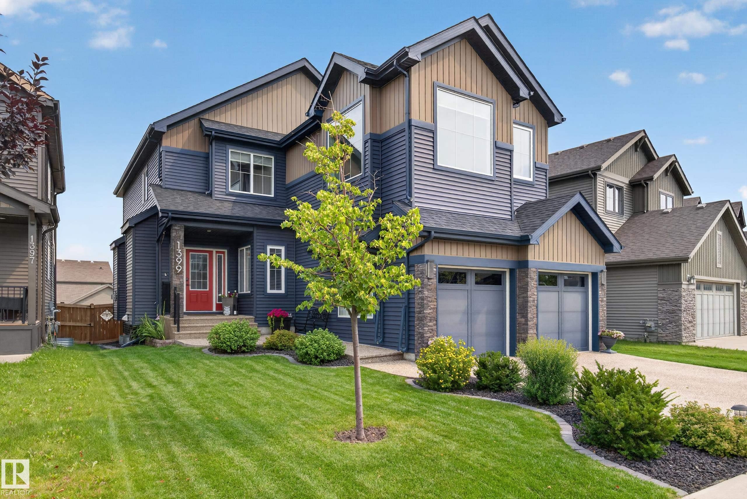 Two-story home with a two-car garage, stone accents, mature landscaping, and a red entry door - 1399 Graydon Hill Way Sw, Edmonton, AB