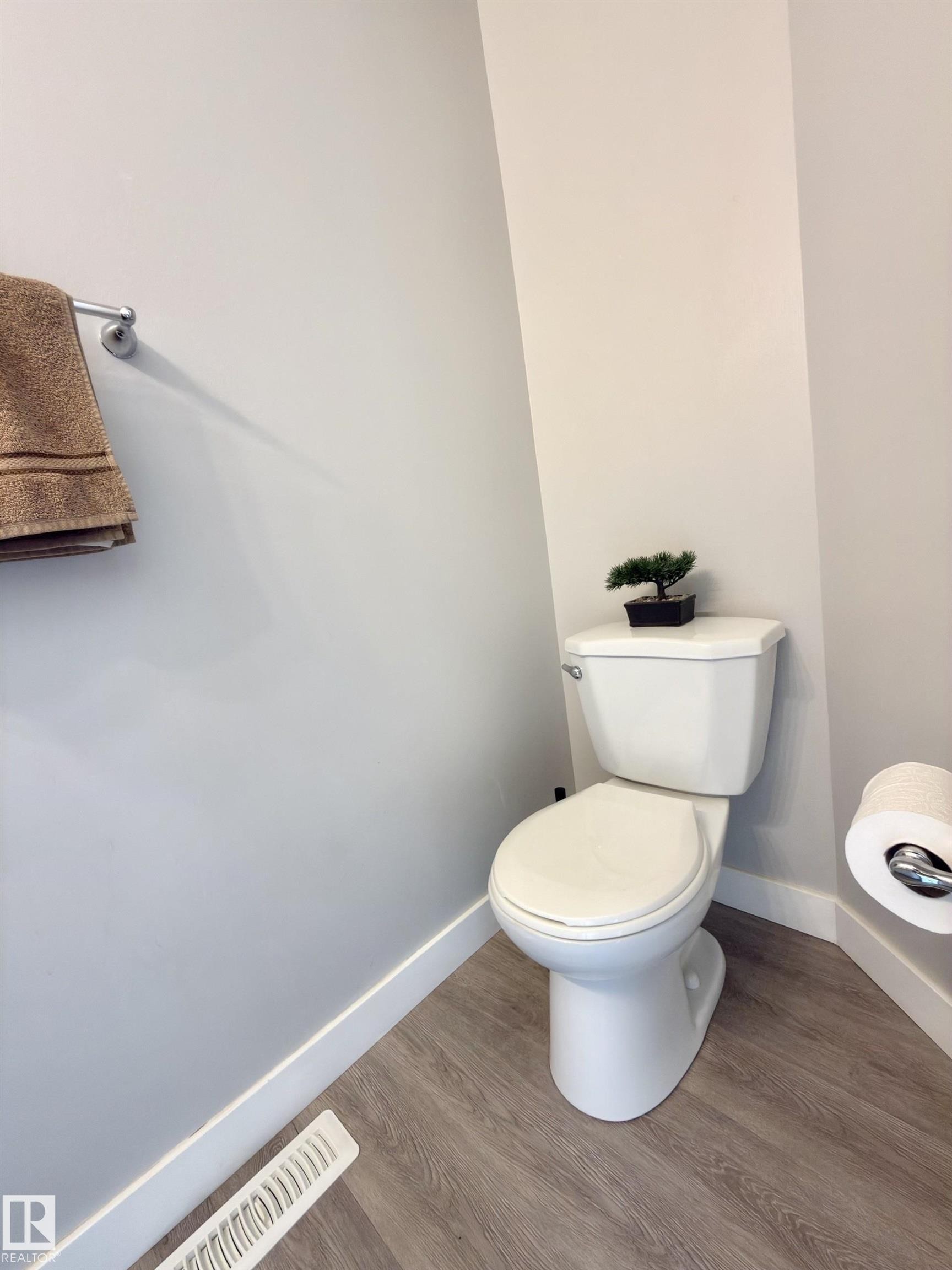Wood-finish flooring, white baseboards, and a white toilet - #13 18010 98 Av Nw Nw, Edmonton, AB - Indoor Photo Showing Bathroom