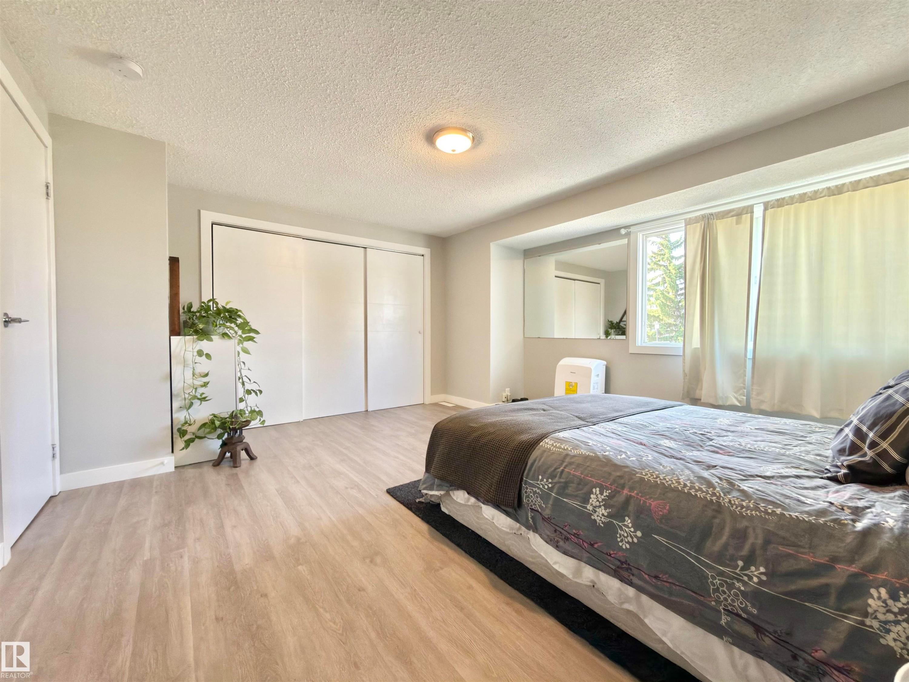 Wood-finish flooring, white sliding closet doors, and a window with natural light - #13 18010 98 Av Nw Nw, Edmonton, AB - Indoor Photo Showing Bedroom