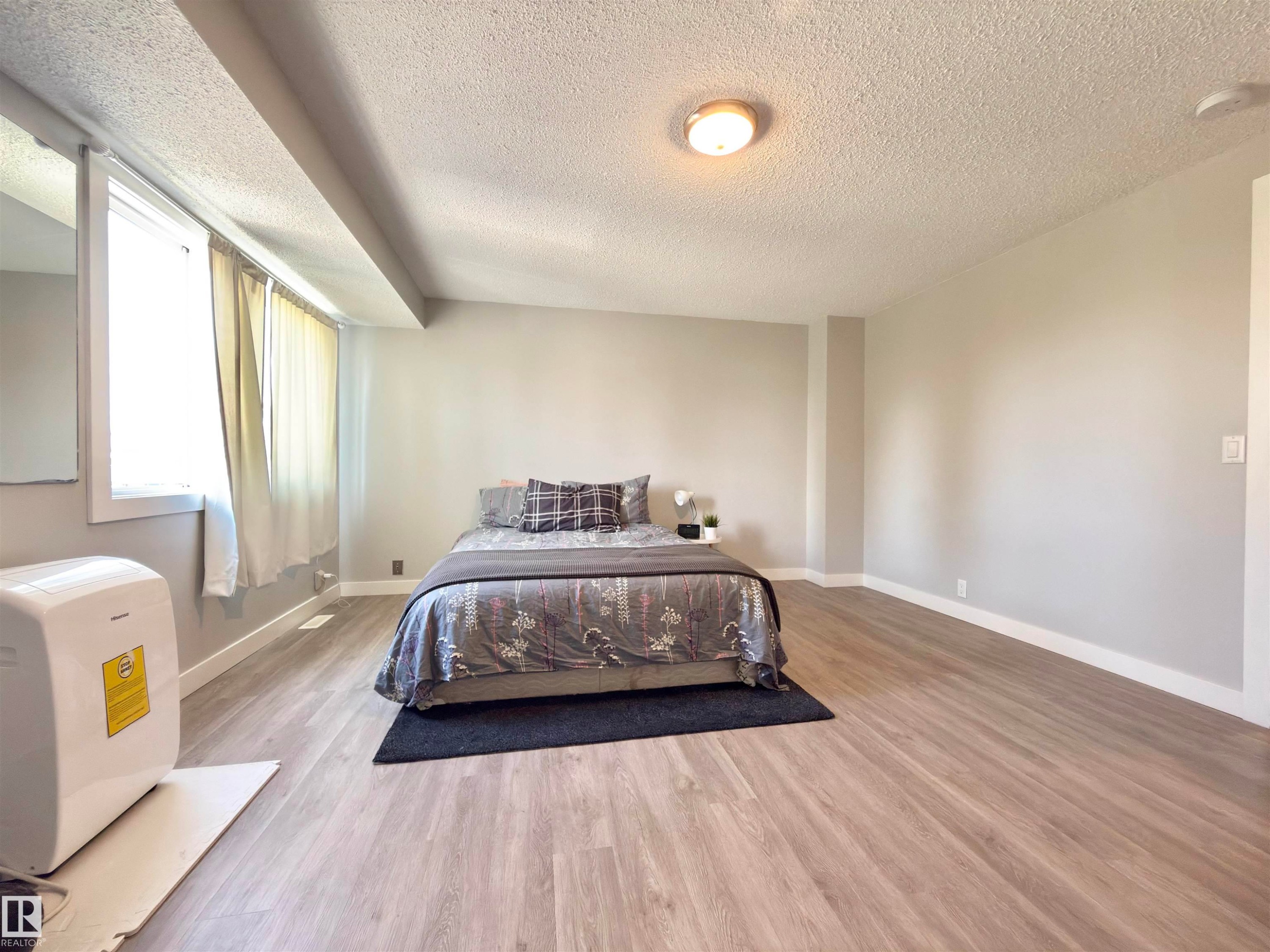 Light wood-finish flooring, neutral wall paint, white trim, and a surface-mounted ceiling light fixture - #13 18010 98 Av Nw Nw, Edmonton, AB - Indoor Photo Showing Bedroom