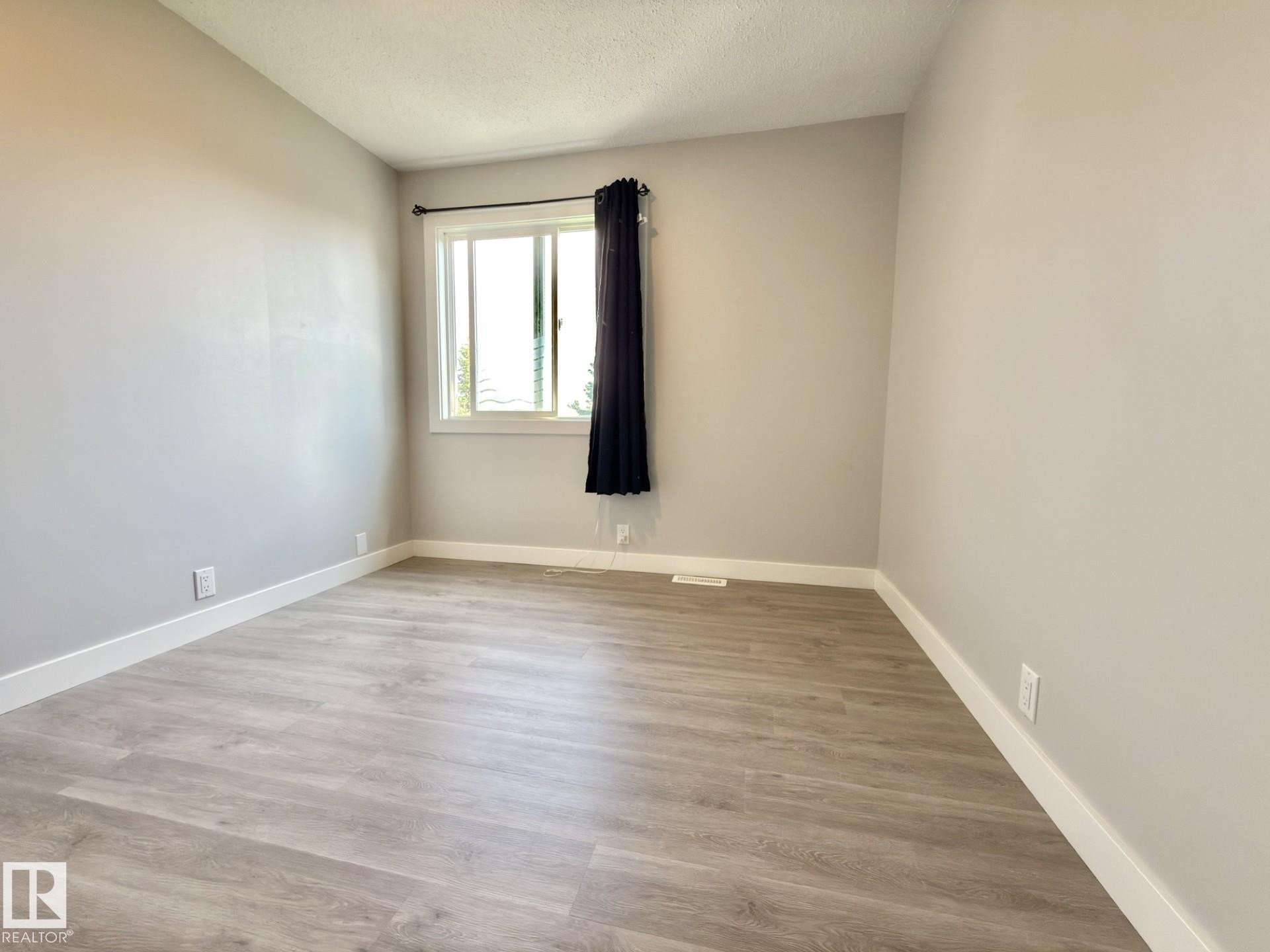 Light gray walls with white trim, wood-finish flooring, and a double-pane window - #13 18010 98 Av Nw Nw, Edmonton, AB - Indoor Photo Showing Other Room