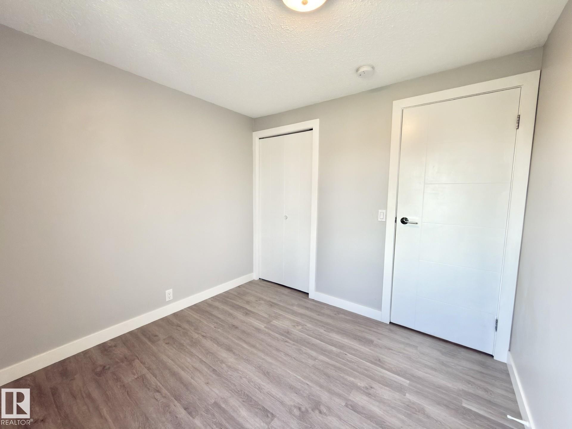Wood-finish flooring, light grey wall paint, and white trim - #13 18010 98 Av Nw Nw, Edmonton, AB - Indoor Photo Showing Other Room