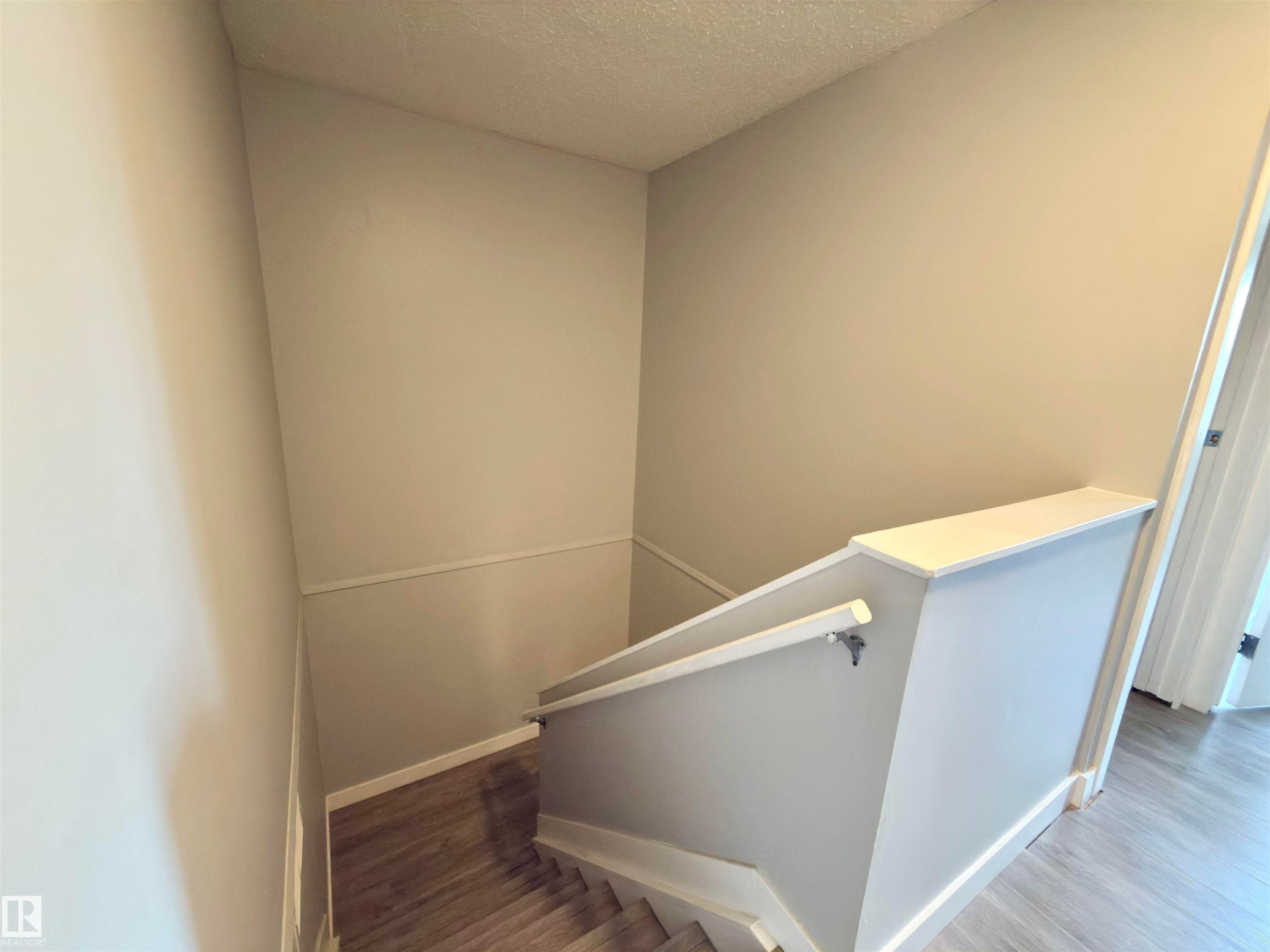 Staircase with wood-finish treads and risers, featuring a light-toned wall and white railing - #13 18010 98 Av Nw Nw, Edmonton, AB - Indoor Photo Showing Other Room