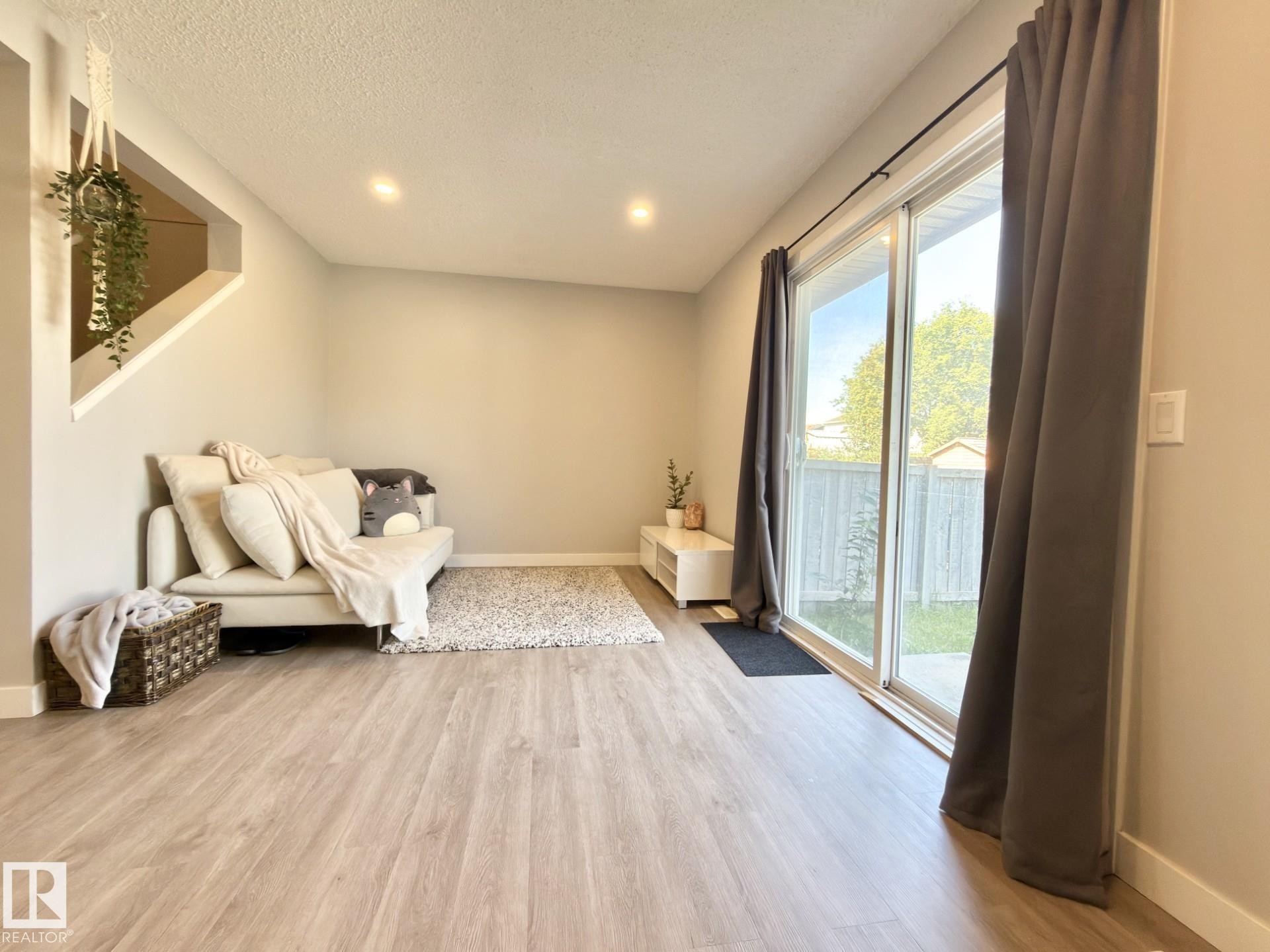 Wood-finish flooring throughout, recessed ceiling lighting, and a sliding glass door leading to the exterior - #13 18010 98 Av Nw Nw, Edmonton, AB - Indoor Photo Showing Other Room