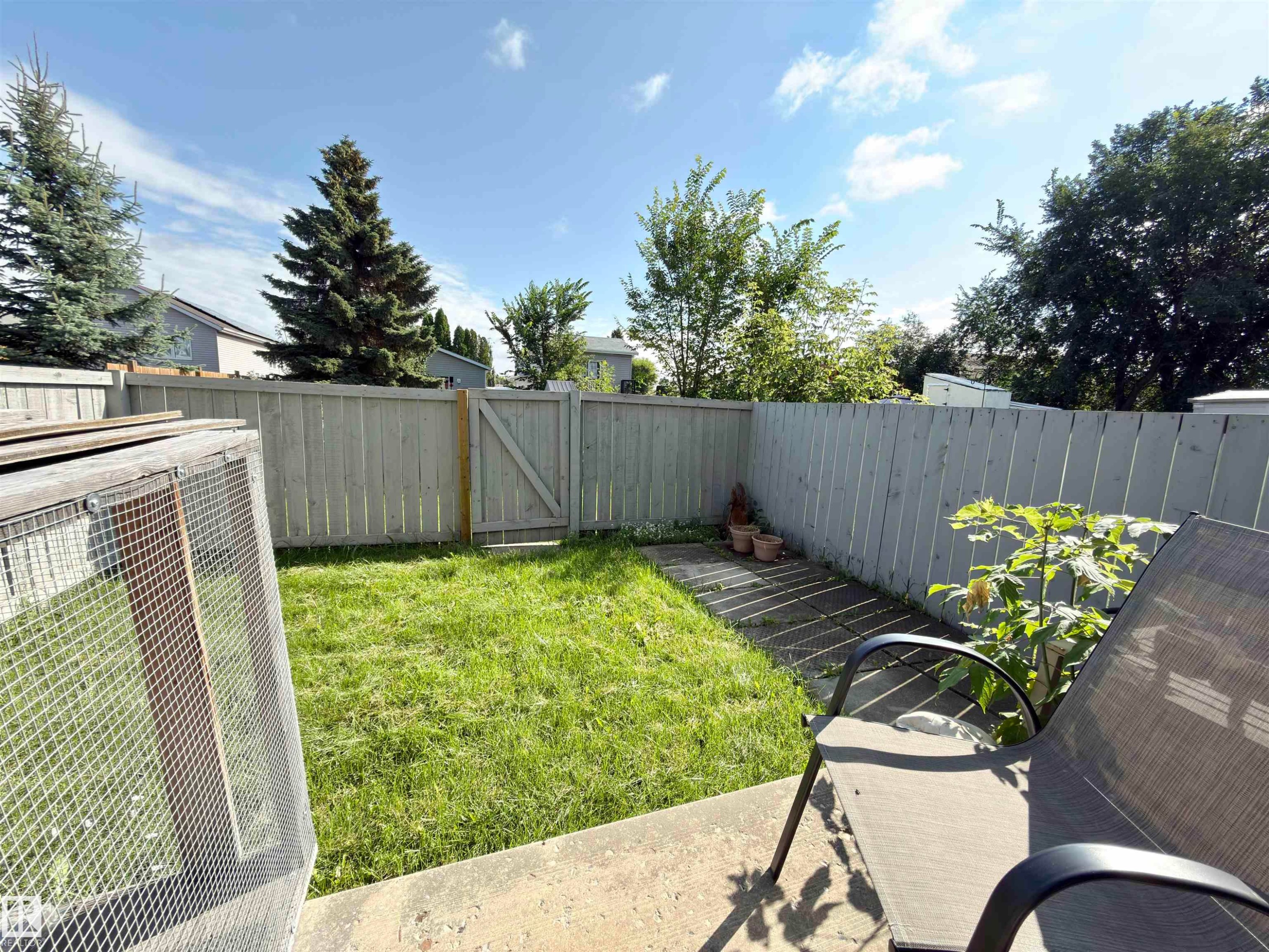 Outdoor patio space featuring a concrete pad, a wooden privacy fence, a wooden gate, and a grass area - #13 18010 98 Av Nw Nw, Edmonton, AB - Outdoor With Backyard