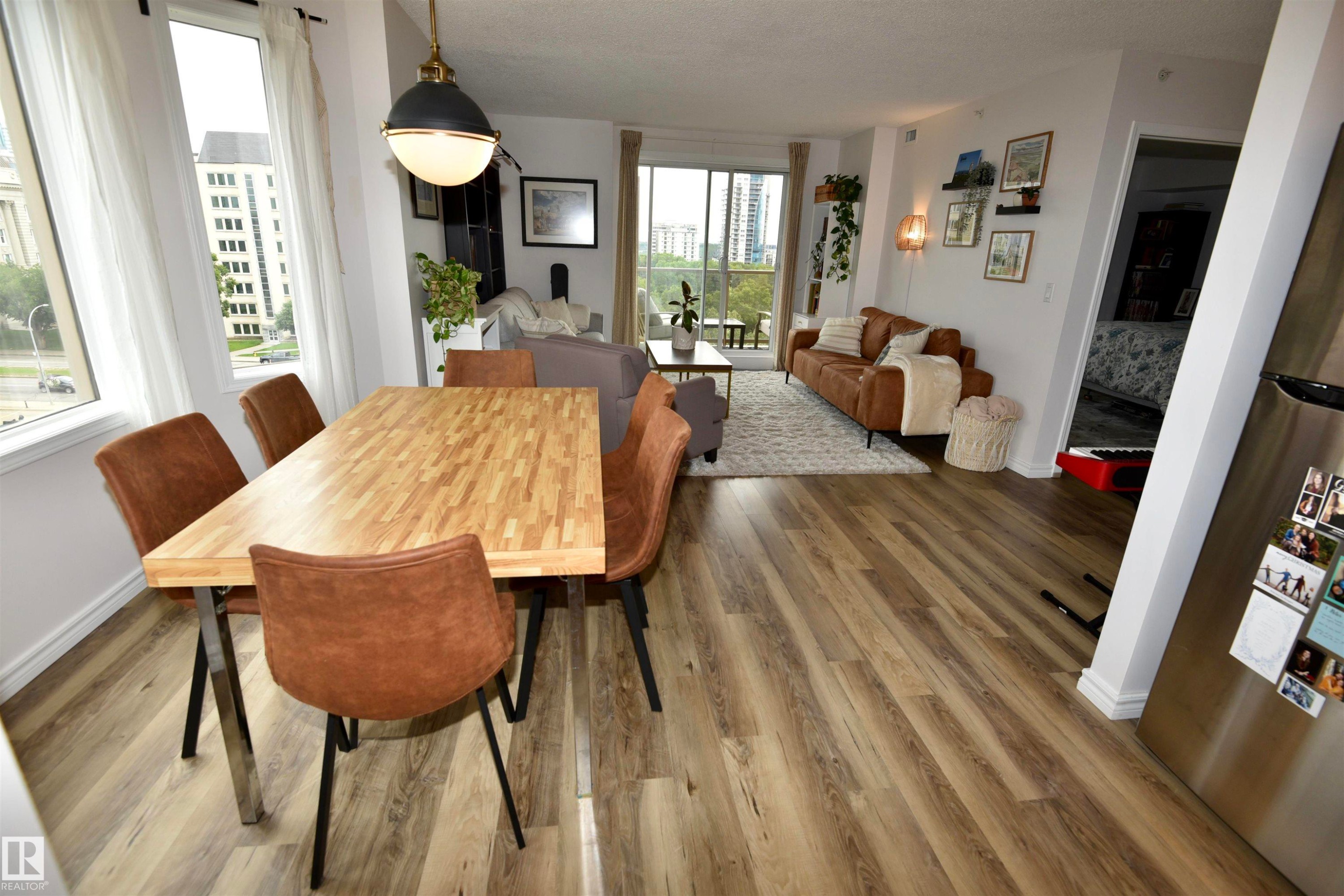 Expansive wood-finish flooring throughout, featuring a dining area with a butcher block style table, a modern pendant light fixture, and large windows - #706 9741 110 St Nw, Edmonton, AB - Indoor Photo Showing Dining Room