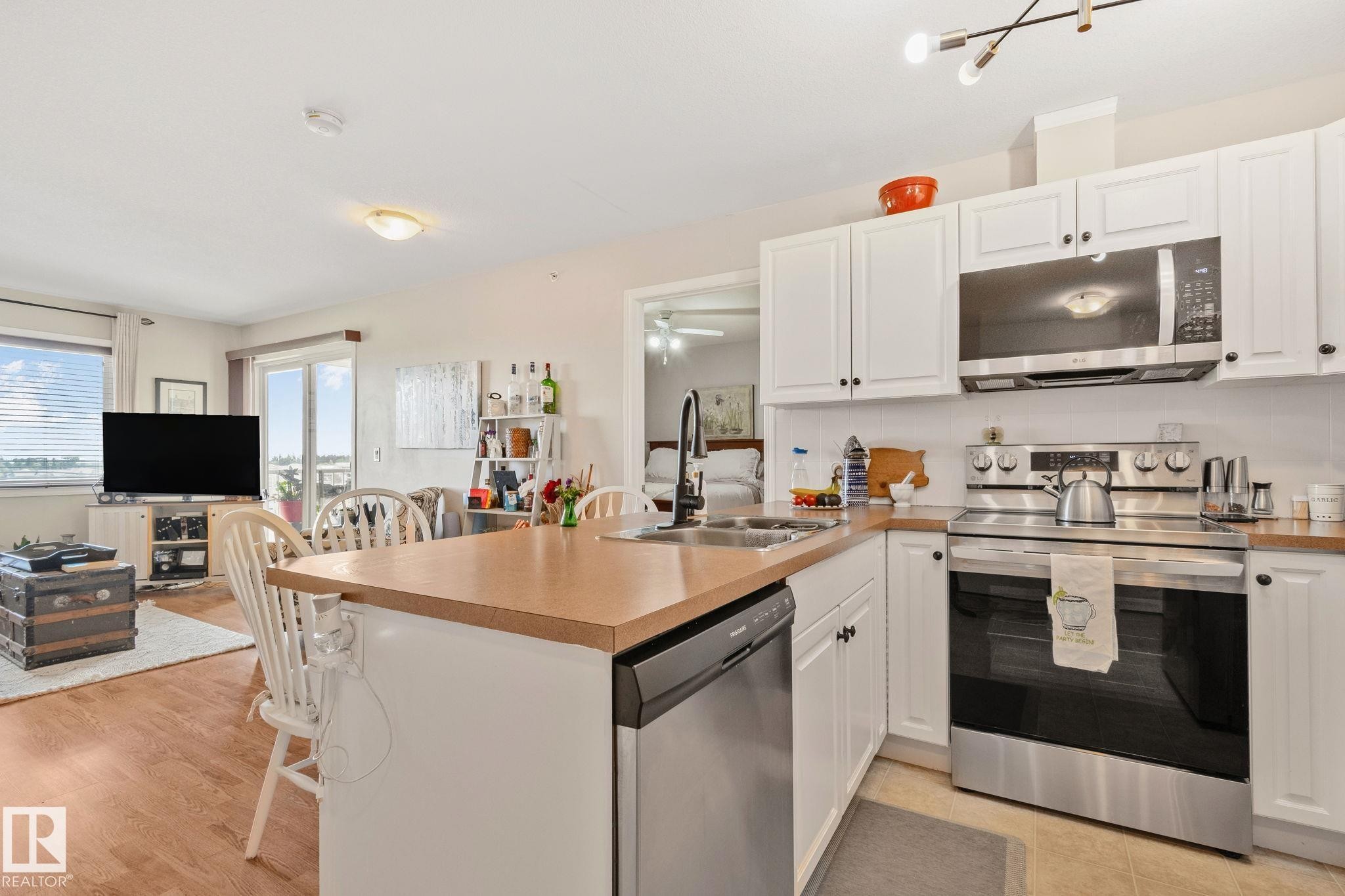 Kitchen island with an integrated sink, stainless steel appliances, white cabinetry, and wood-finish countertops - #407 4309 33 St, Stony Plain, AB - Indoor Photo Showing Kitchen With Double Sink