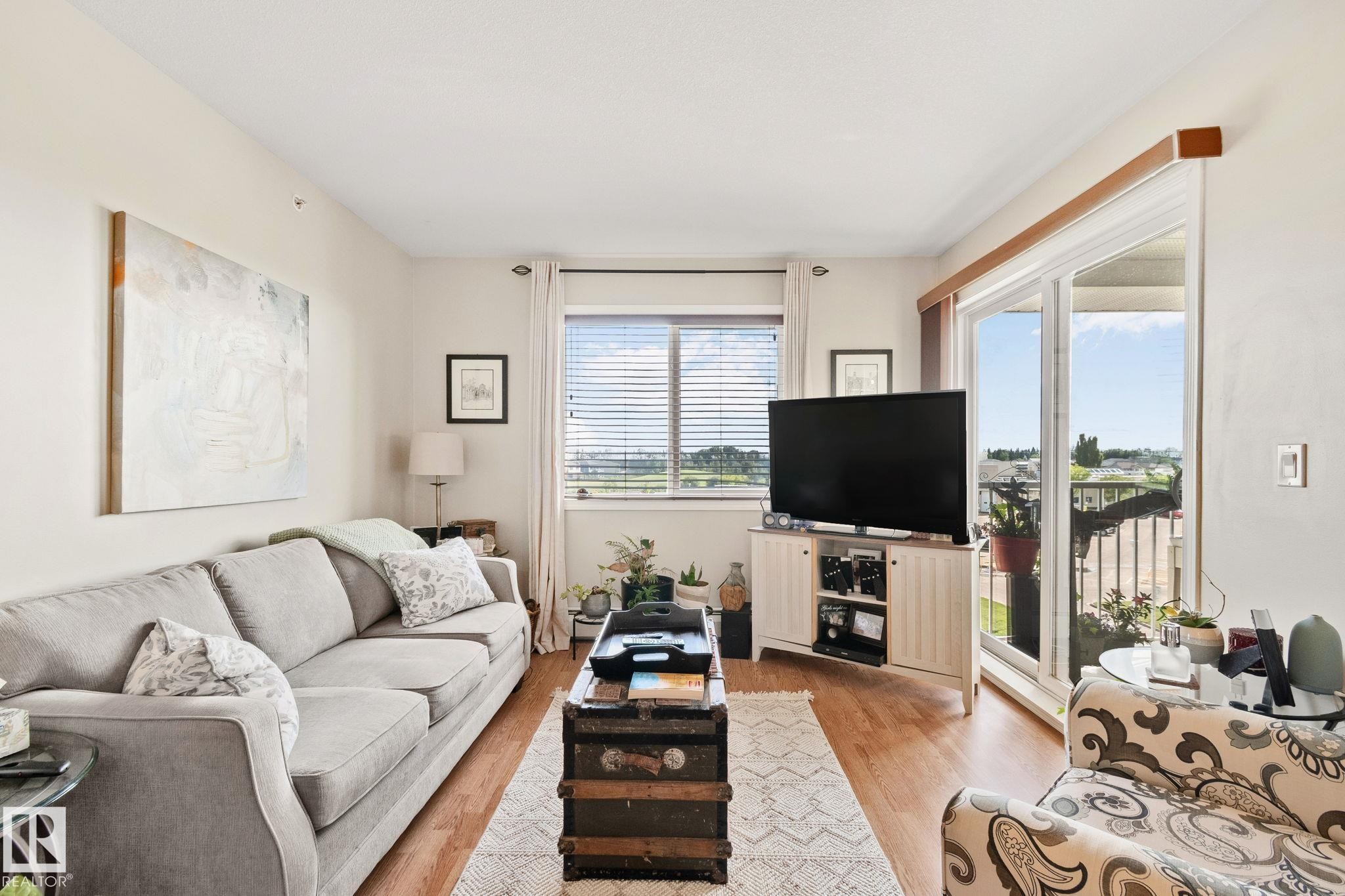 Light wood-finish flooring, white painted walls, window with blinds, and white-framed sliding glass door - #407 4309 33 St, Stony Plain, AB - Indoor Photo Showing Living Room