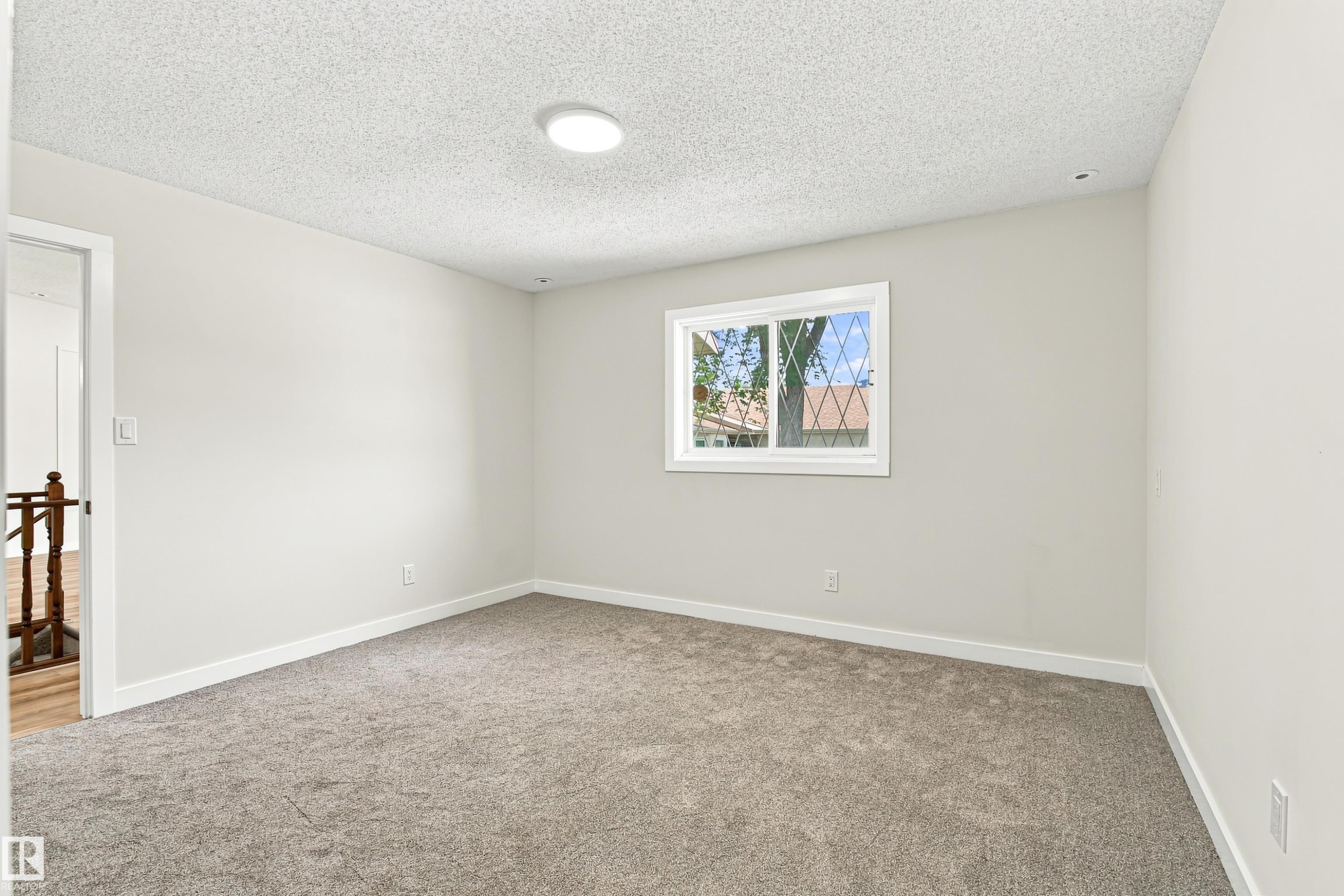 Wall-to-wall carpeting, white interior walls, overhead flush-mount lighting, and a window with white casing - #21 9375 172 St Nw, Edmonton, AB - Indoor Photo Showing Other Room