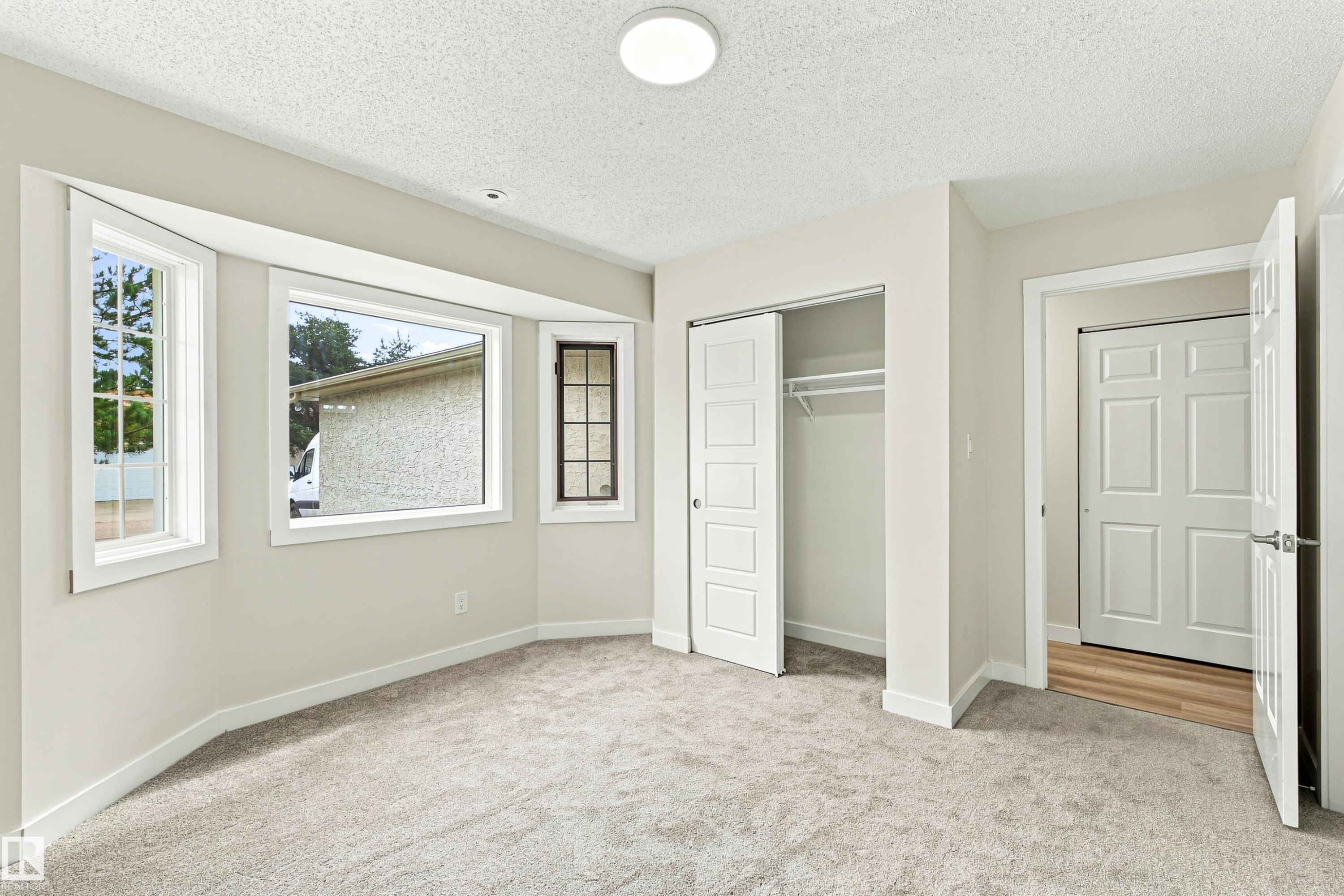 Recessed bay window, light grey carpeting, white trim, sliding closet doors, and a flush mount ceiling light - #21 9375 172 St Nw, Edmonton, AB - Indoor Photo Showing Other Room