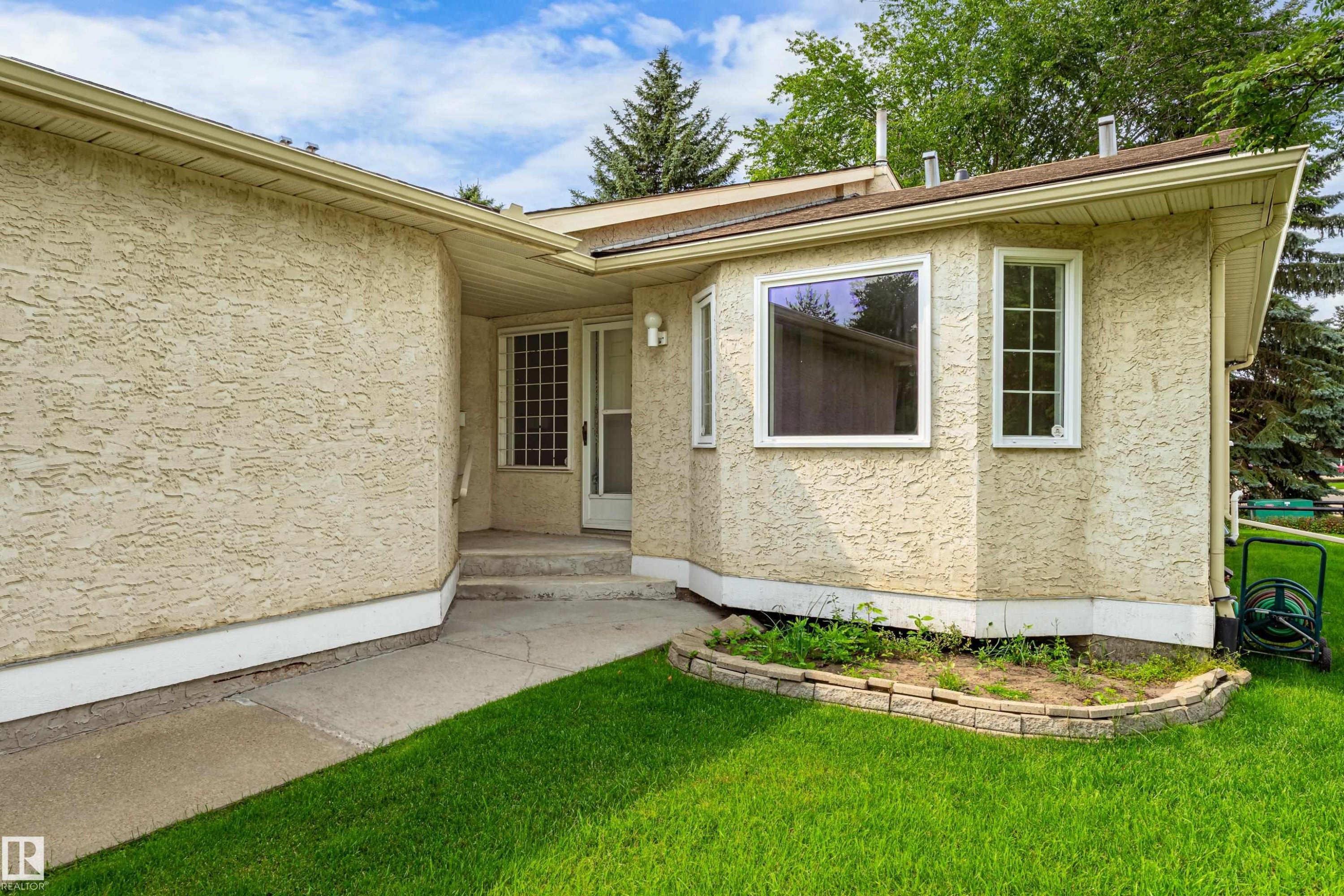 Stucco exterior with a bay window design, concrete pathway, and a landscaped garden bed - #21 9375 172 St Nw, Edmonton, AB - Outdoor