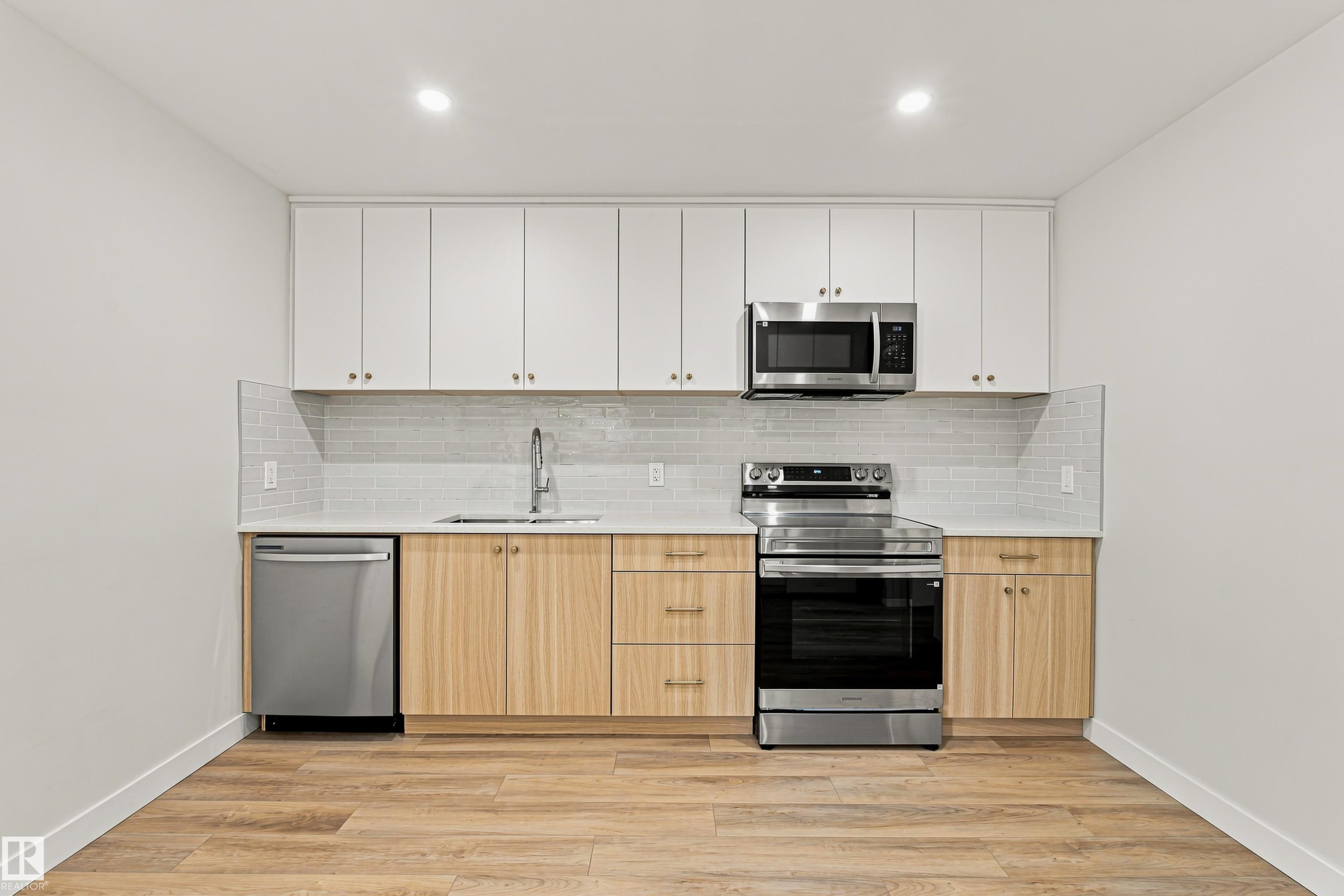 Stainless steel appliances, wood-finish flooring, light wood-finish lower cabinetry, white upper cabinetry, and a tile backsplash - #21 9375 172 St Nw, Edmonton, AB - Indoor Photo Showing Kitchen