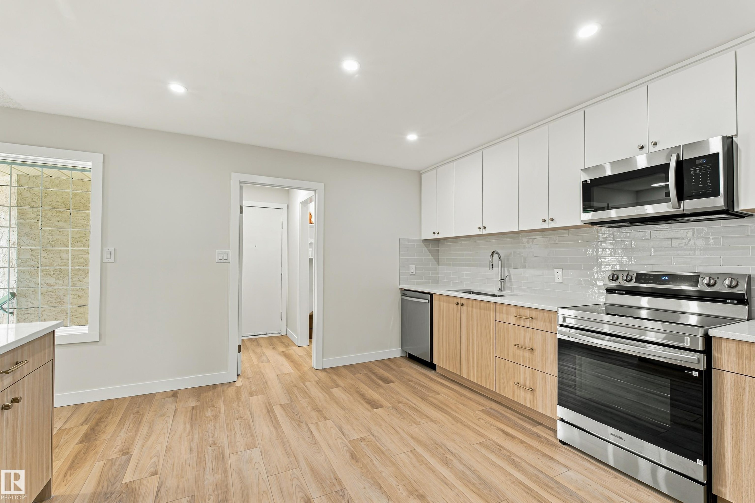 Kitchen featuring wood-finish flooring, two-tone cabinetry, stainless steel appliances, a tile backsplash, and recessed lighting - #21 9375 172 St Nw, Edmonton, AB - Indoor Photo Showing Kitchen