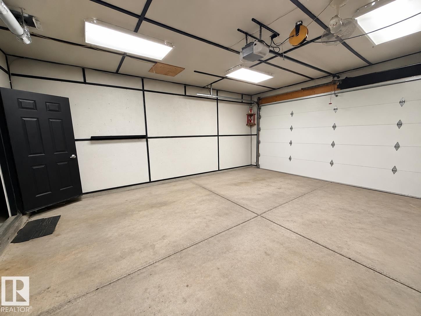 Concrete flooring, overhead fluorescent lighting, paneled walls, and a white overhead garage door - 3512 11 Street Nw, Edmonton, AB