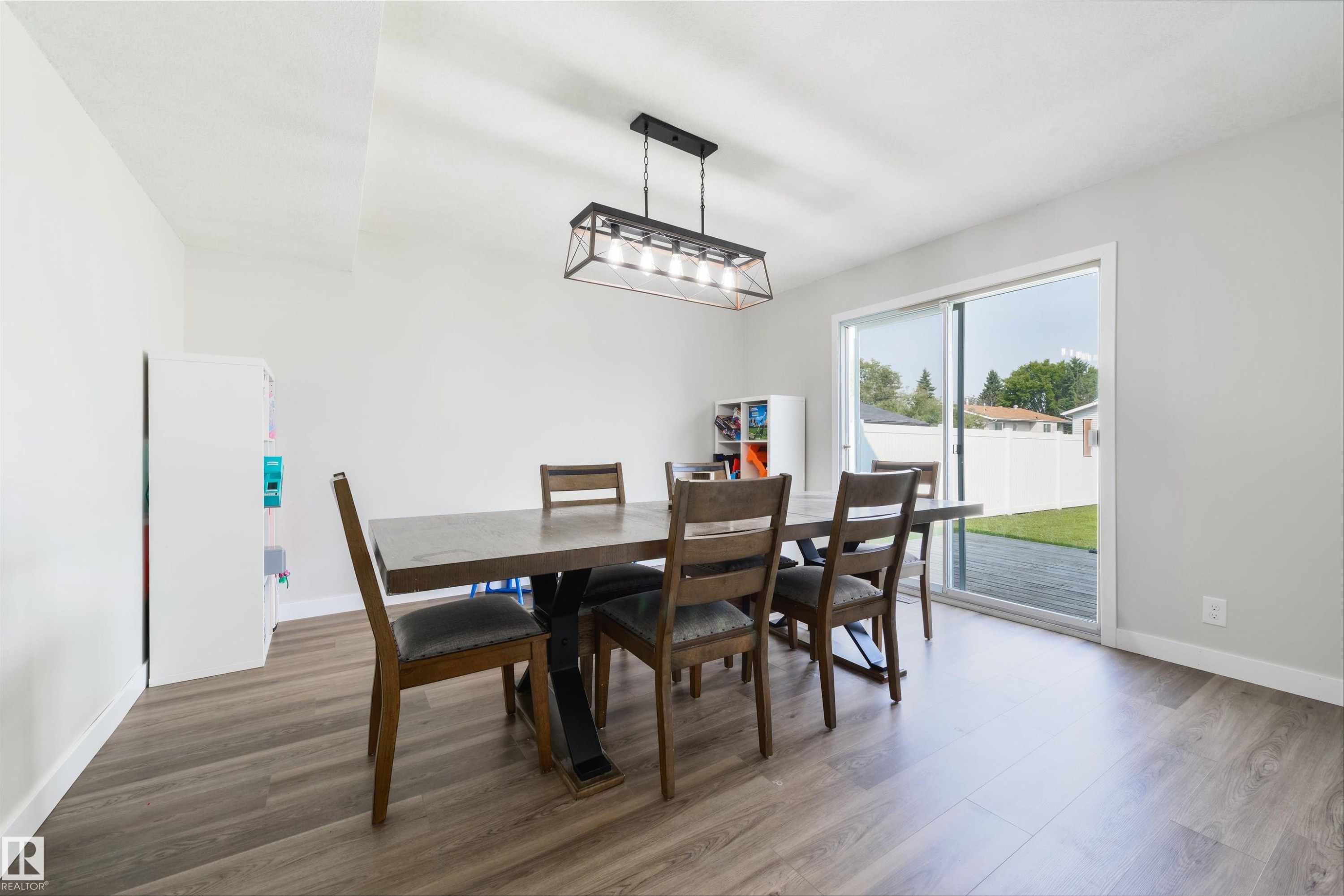 Wood-finish flooring, white walls, and a contemporary linear chandelier with a metal frame - 4614 53 Ave, Calmar, AB - Indoor Photo Showing Dining Room